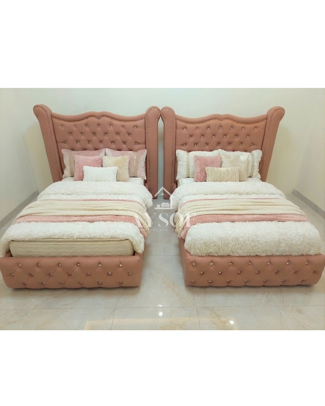 A set of two single beds in blush pink leatherette, with tall wingback headboards, crystal buttons, and tufted footboards. Elegant, matching, and perfect for shared rooms.