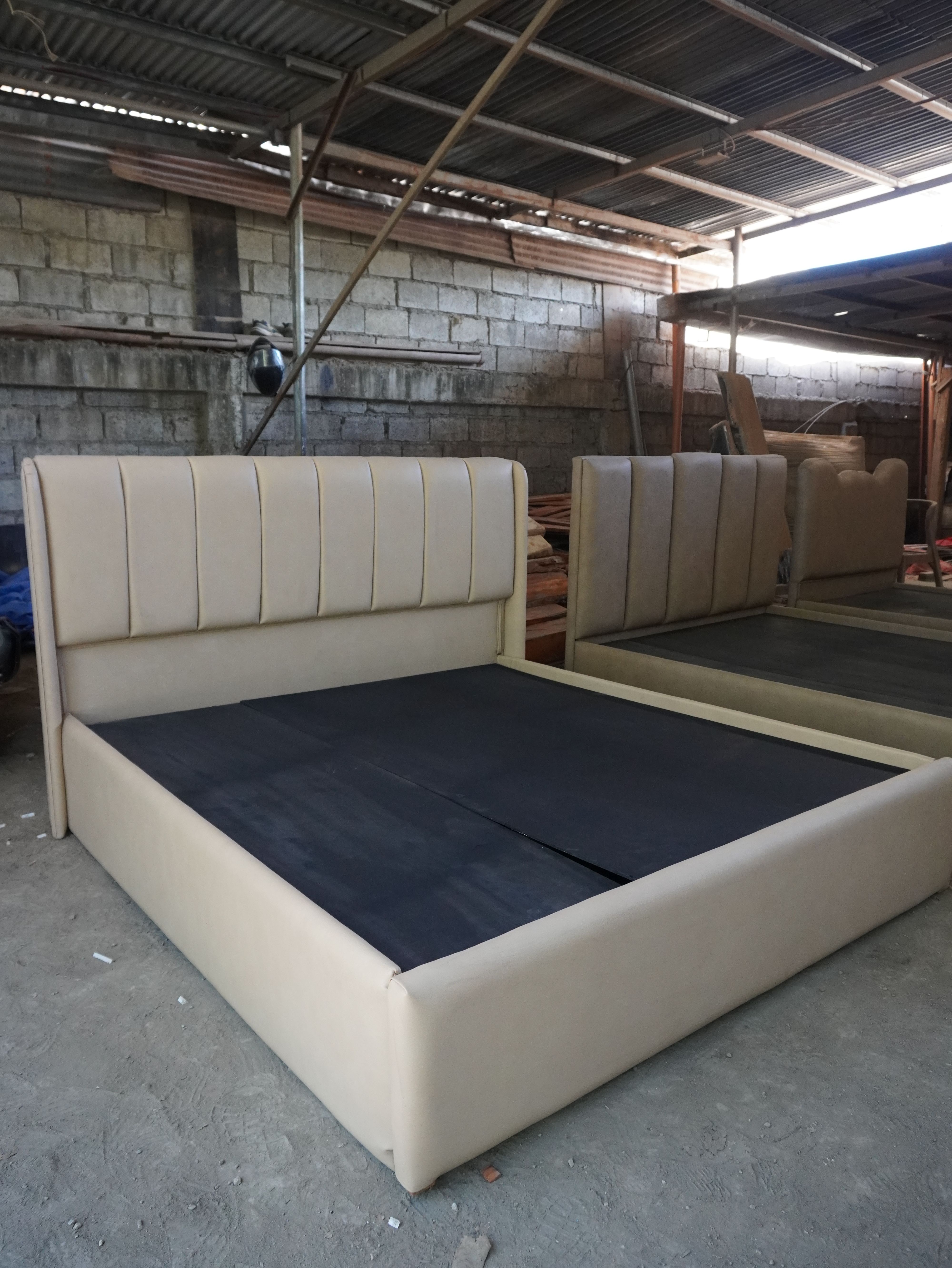A clean, tailored upholstered bed in soft latte-beige leatherette, with a tall vertical channel headboard that wraps into subtle side wings and a smooth, fully wrapped frame. Easy to wipe clean.