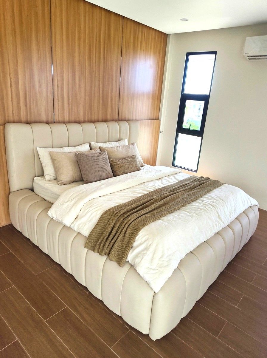 A soft, sculptural bed in smooth cream leatherette, with a tall wide channel headboard and thick pillow-style channels wrapping the whole frame. Plush, modern, and easy to wipe clean.