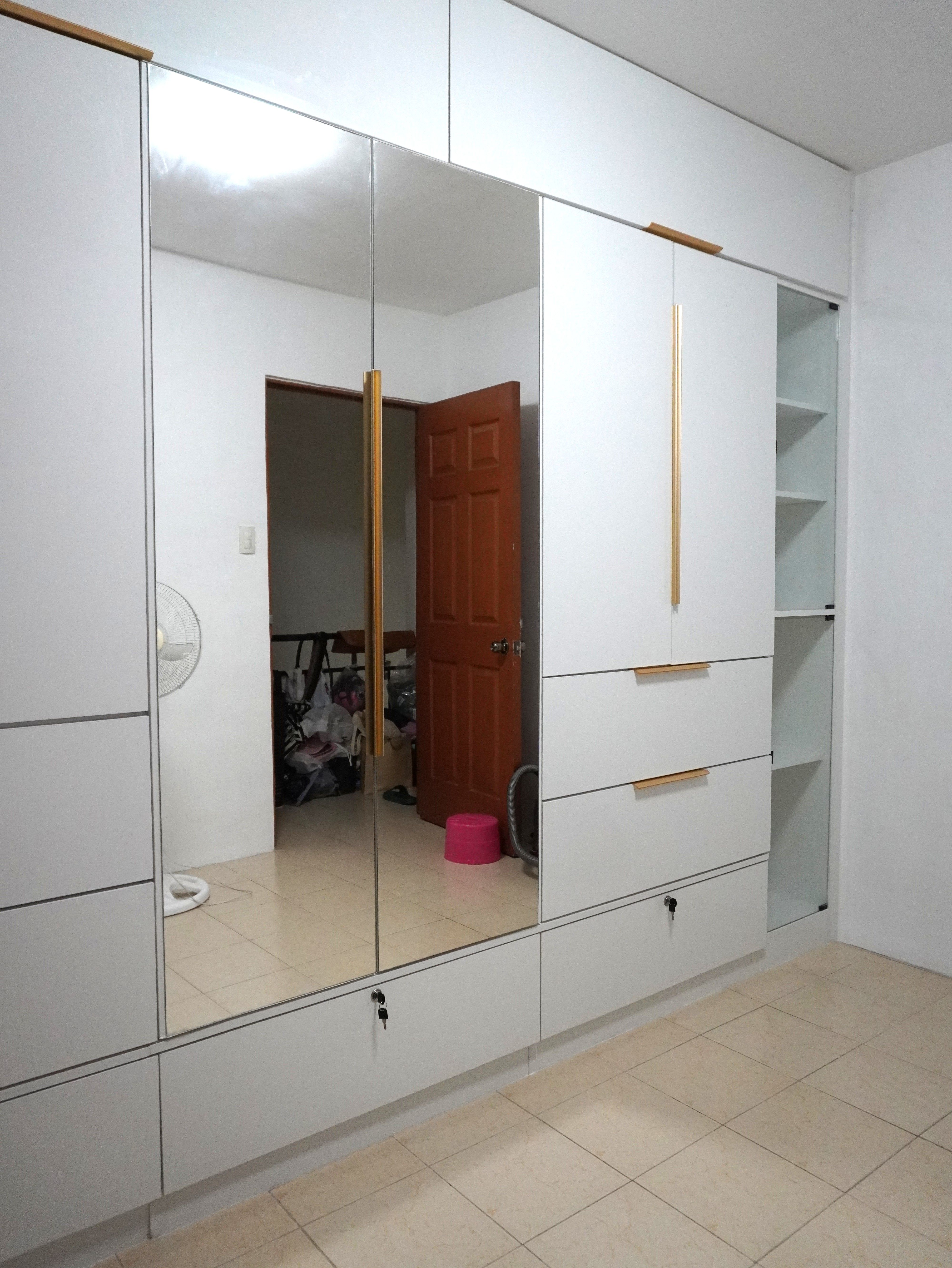 A floor-to-ceiling built-in wardrobe in high-gloss white, with gold bar handles, a full-height center mirror, roomy drawers, three locking drawers, and glass-door shelving. Made to fit your wall.
