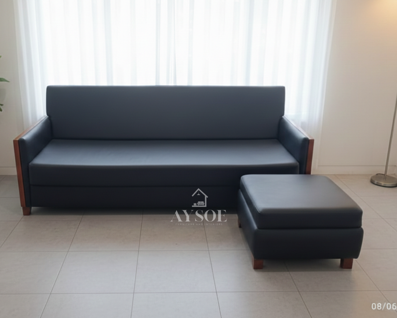 A sleek black leatherette three-seater sofa with cherry wood side panels, wood block legs, and a matching square ottoman. Clean lines, wipe-clean upholstery, made to order.