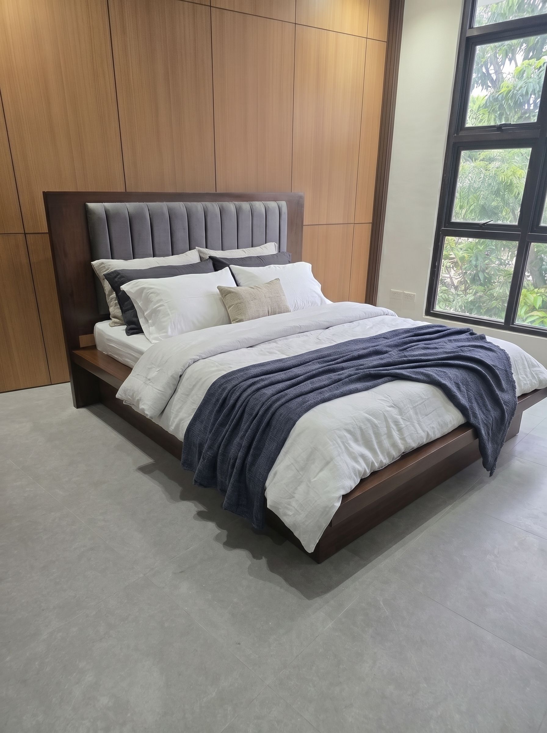 A modern dark walnut platform bed with a wide wood ledge, a recessed base for a floating look, and a tall wood headboard with a soft gray channel-tufted panel. Clean, solid, and built to last.