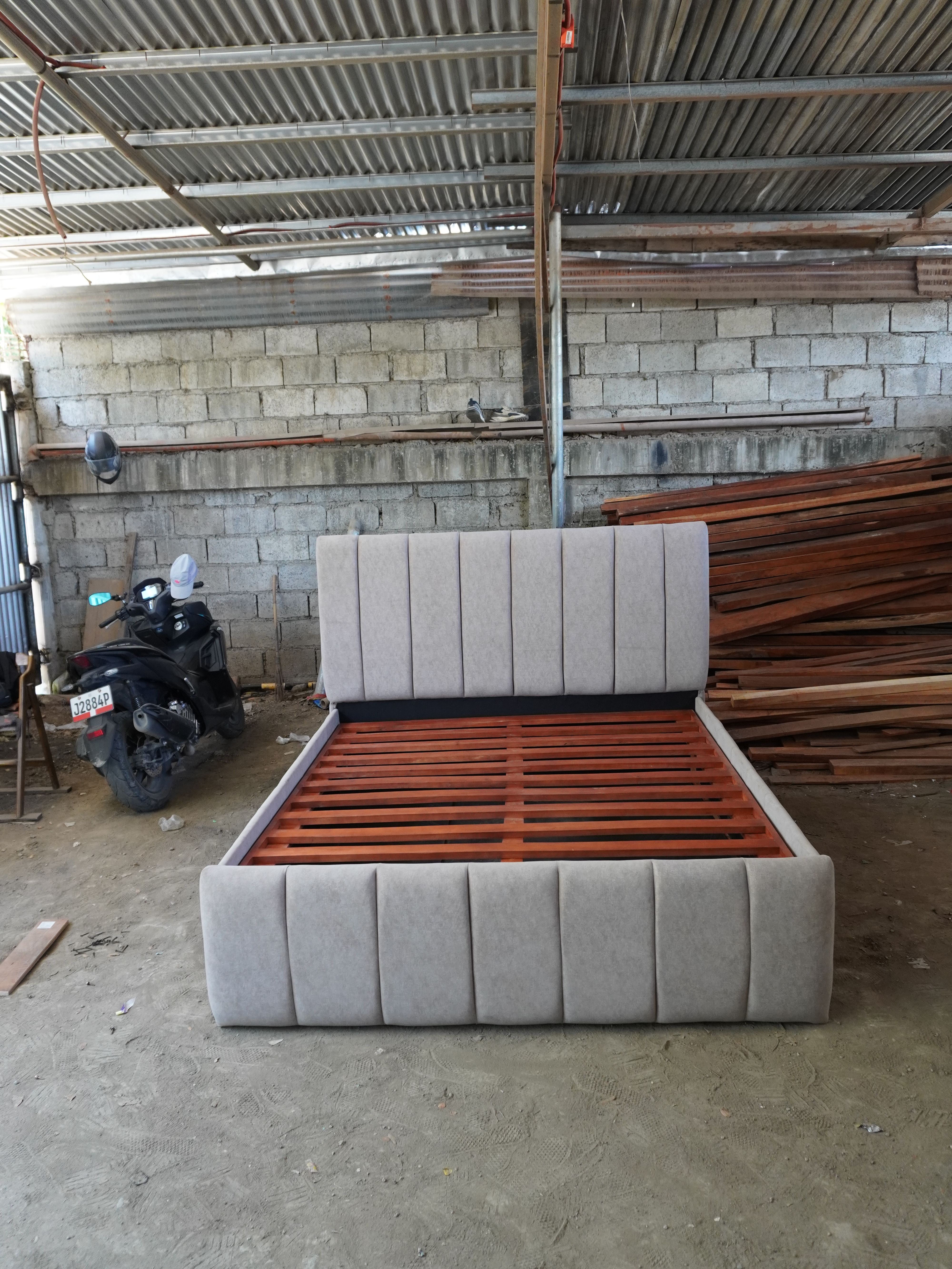 A modern upholstered bed in soft light gray fabric, with vertical channel panels on the headboard and footboard. The gas-lift slatted base opens to one large under-bed storage space.