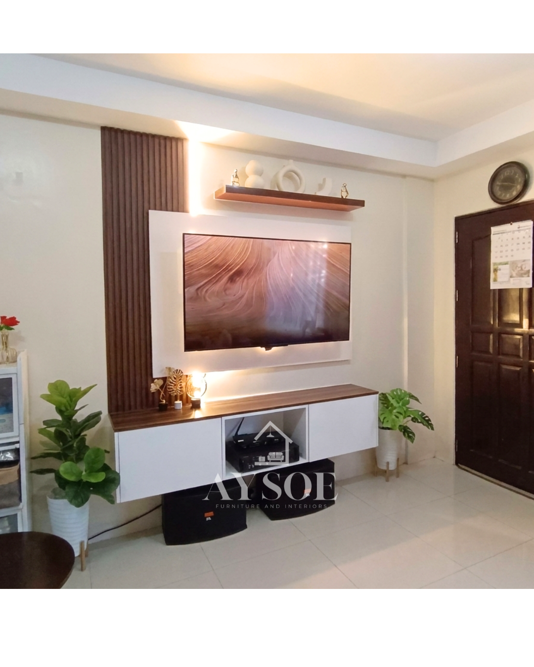A custom TV wall unit with a white backing panel, a walnut fluted accent, a floating shelf, and a wall-mounted cabinet. Modern, tidy, and lit with warm LEDs.