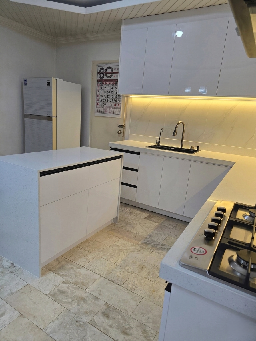 A high-gloss white L-shaped kitchen with a marble-look backsplash, LED lighting, and a waterfall island.