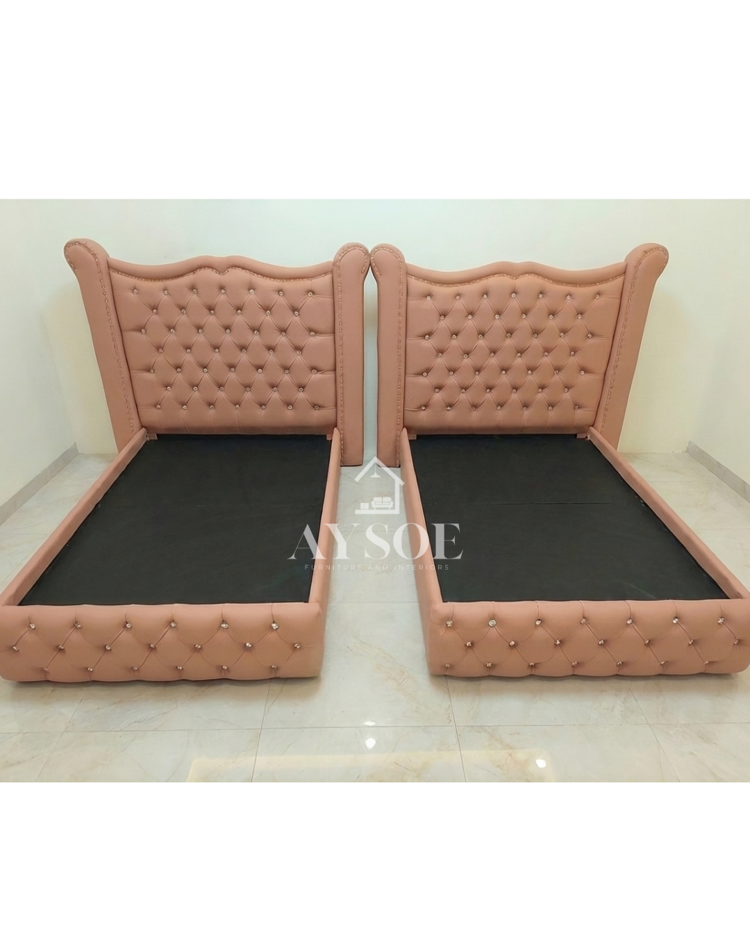 A set of two single beds in blush pink leatherette, with tall wingback headboards, crystal buttons, and tufted footboards. Elegant, matching, and perfect for shared rooms.