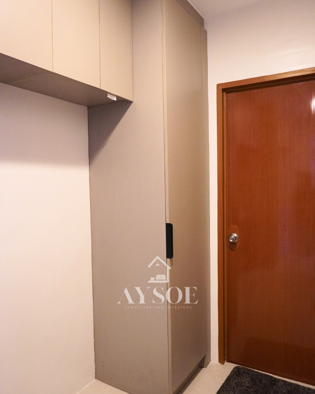 A custom taupe linen-finish storage set with a tall pull-out pantry with six wire baskets and handleless overhead cabinets. Organized storage for kitchens and utility areas.
