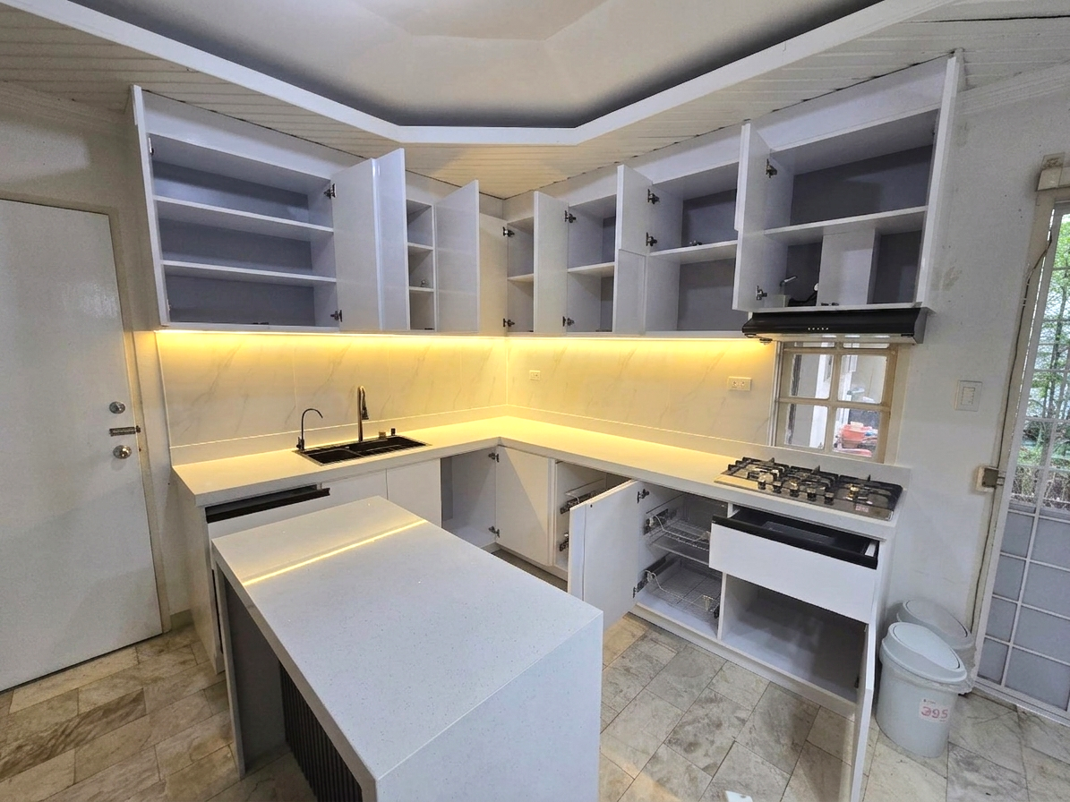 A high-gloss white L-shaped kitchen with a marble-look backsplash, LED lighting, and a waterfall island.