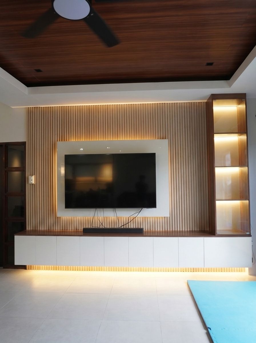 A built-in TV wall with a vertical wood-slat feature panel, a white gloss TV backing, a long floating storage cabinet, and a tall glass-door display tower. Warm LED lighting makes it glow. Made to fit your wall.