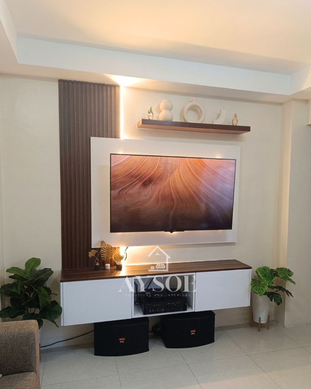 A custom TV wall unit with a white backing panel, a walnut fluted accent, a floating shelf, and a wall-mounted cabinet. Modern, tidy, and lit with warm LEDs.