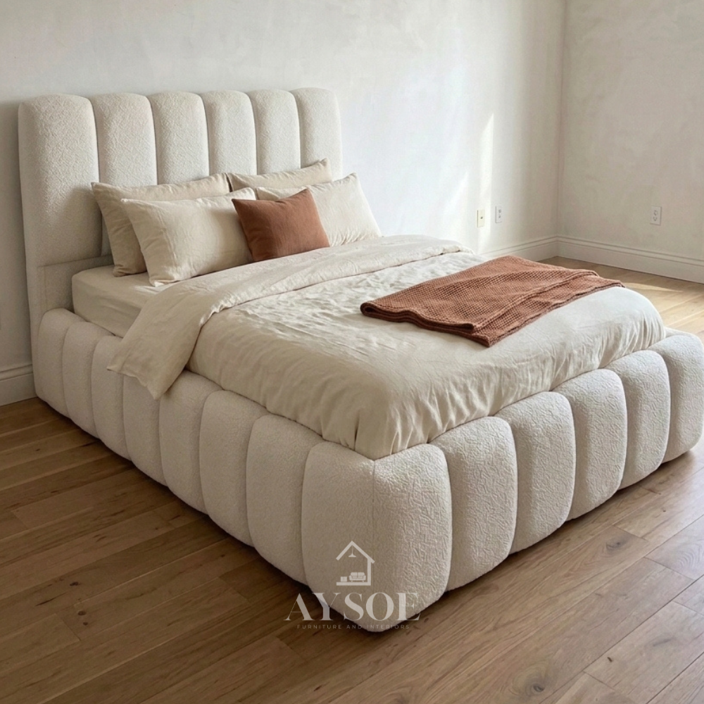 A soft, sculptural bed in ivory bouclé fabric, with a tall rounded channel headboard and thick pillow-style channels wrapping the whole frame. Cozy, modern, and a real statement piece.