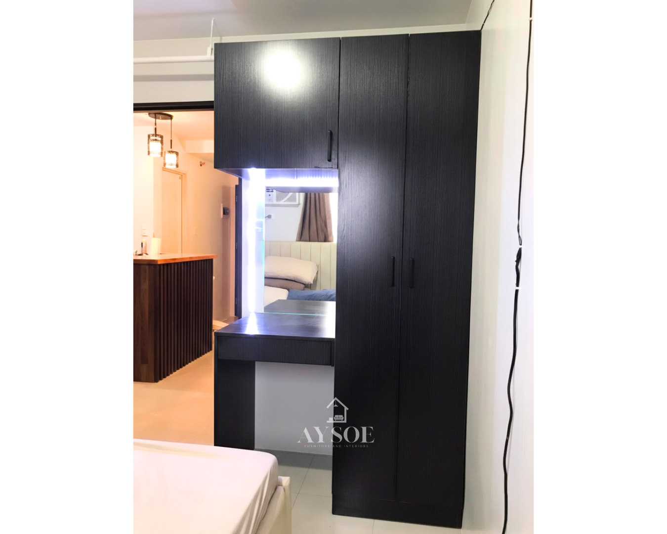 A custom black wood-grain wardrobe with a built-in vanity table, an LED-lit mirror, and an overhead cabinet. Smart storage and a grooming corner in one compact unit.