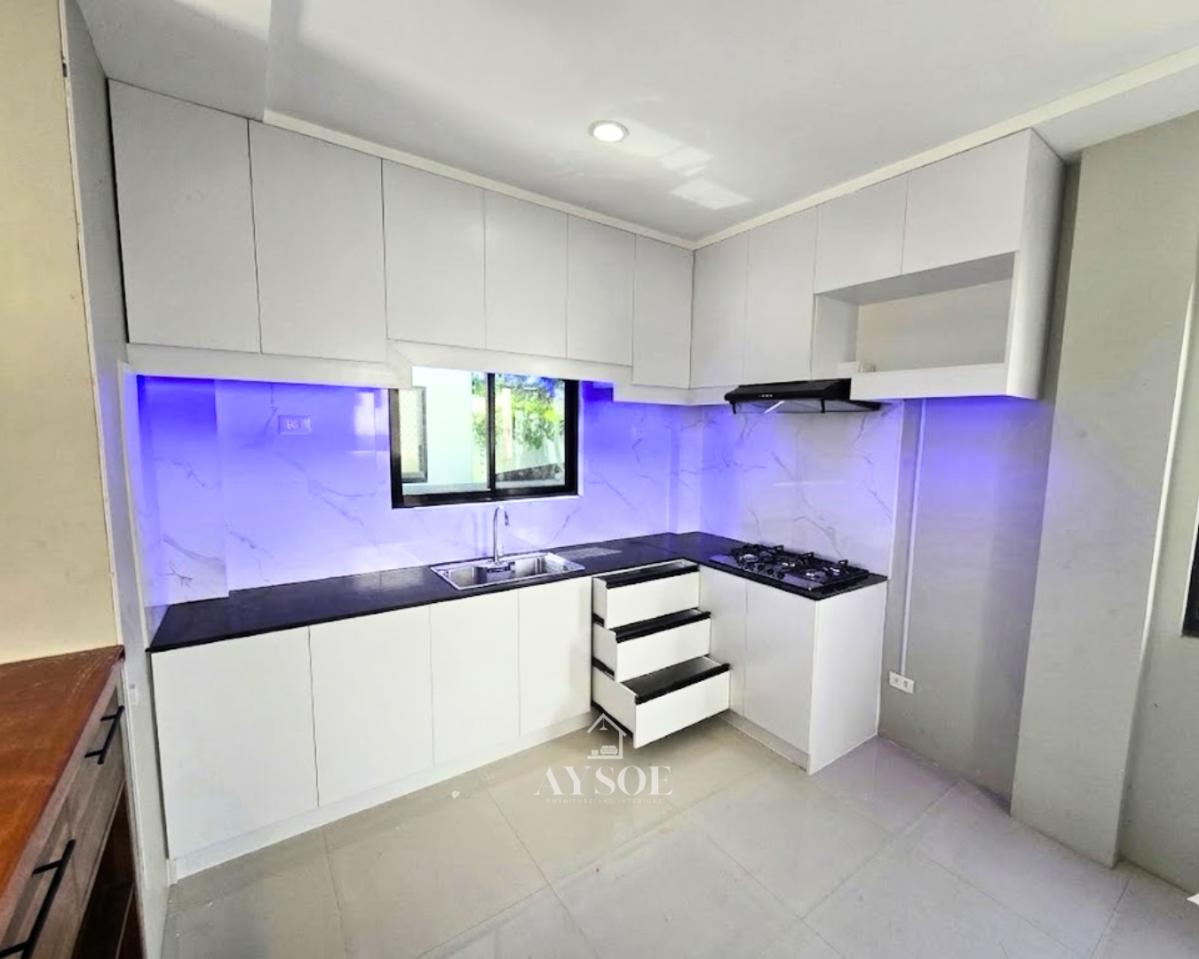 A modern L-shaped kitchen set with glossy white cabinets, a dark countertop, a marble-look backsplash, and a wood island counter with drawers. Plenty of storage in a clean, bright design.