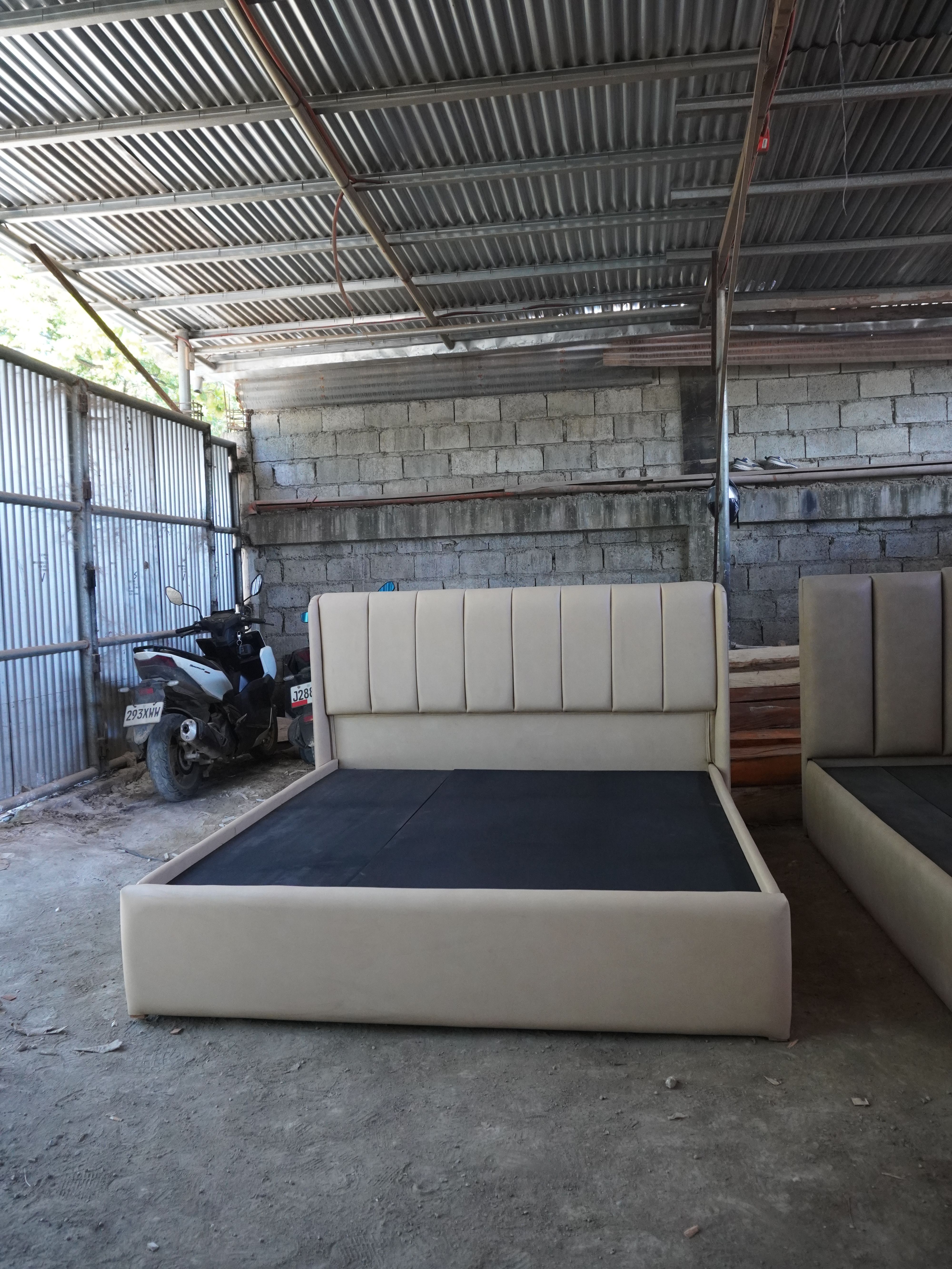 A clean, tailored upholstered bed in soft latte-beige leatherette, with a tall vertical channel headboard that wraps into subtle side wings and a smooth, fully wrapped frame. Easy to wipe clean.