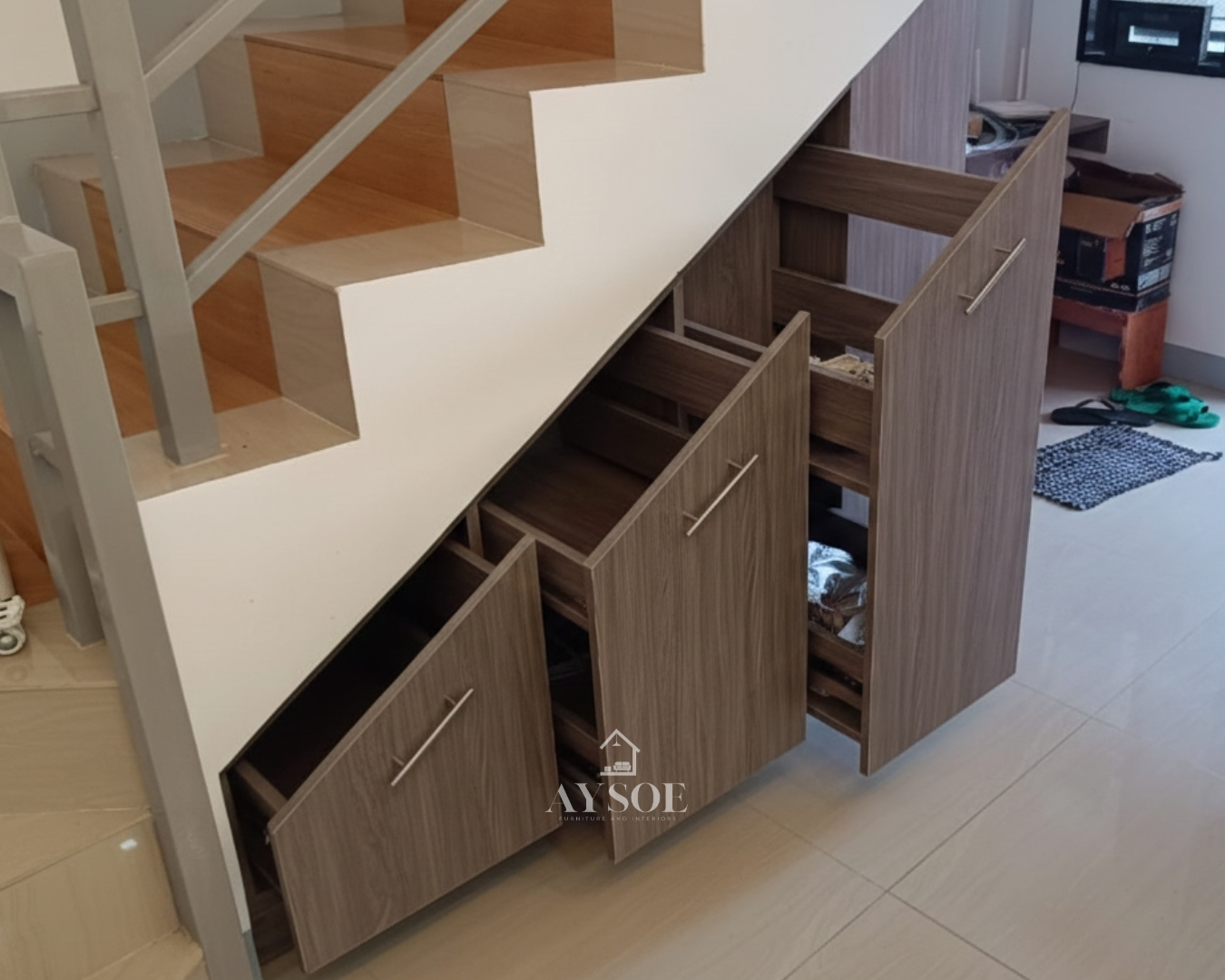 A custom under-stair storage cabinet with three deep pull-out drawers in a grey-brown wood-grain finish. Turns unused stair space into organized storage.