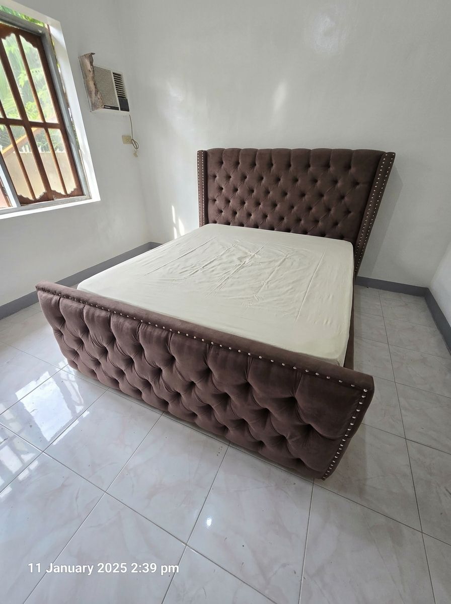 A classic, chocolate brown upholstered bed frame featuring deep tufted button detailing on both the high headboard and the footboard. The edges are accented with a silver nailhead trim.