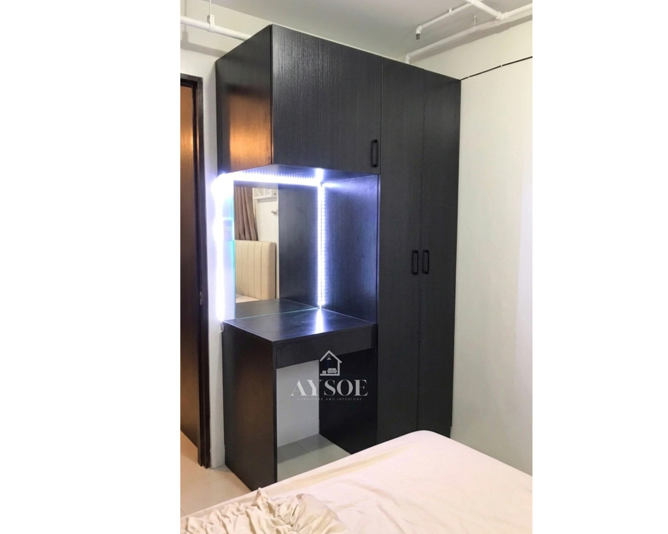 A custom black wood-grain wardrobe with a built-in vanity table, an LED-lit mirror, and an overhead cabinet. Smart storage and a grooming corner in one compact unit.