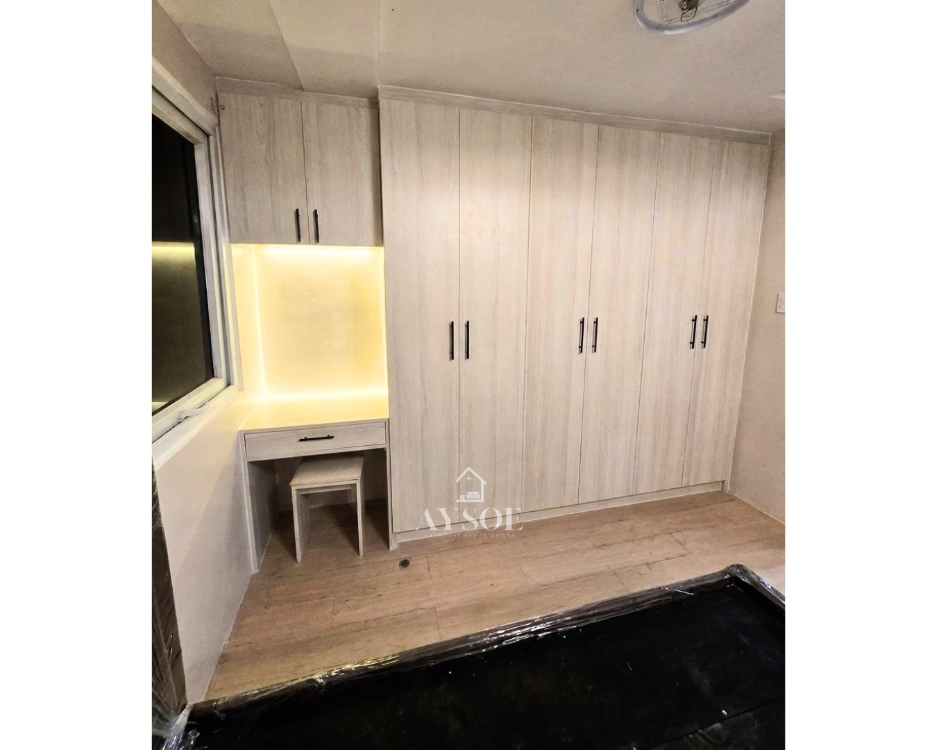 A custom light oak wardrobe with six full-height doors, a built-in vanity desk with LED lighting, and an overhead cabinet. Lots of storage in one clean design.