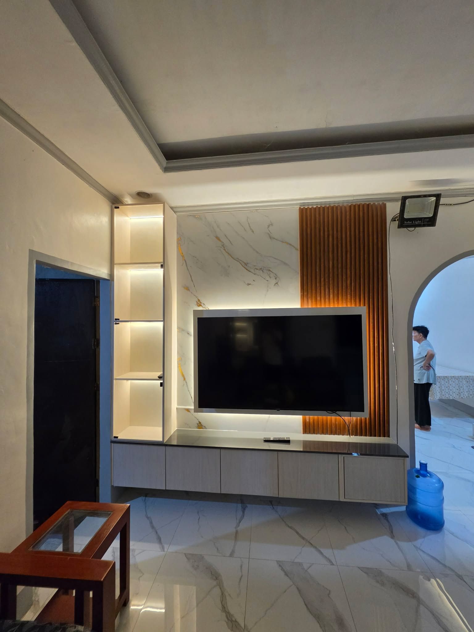 Modern TV feature wall with warm ambient lighting, a marble-look backdrop, wood slat accents, and sleek floating storage cabinets.