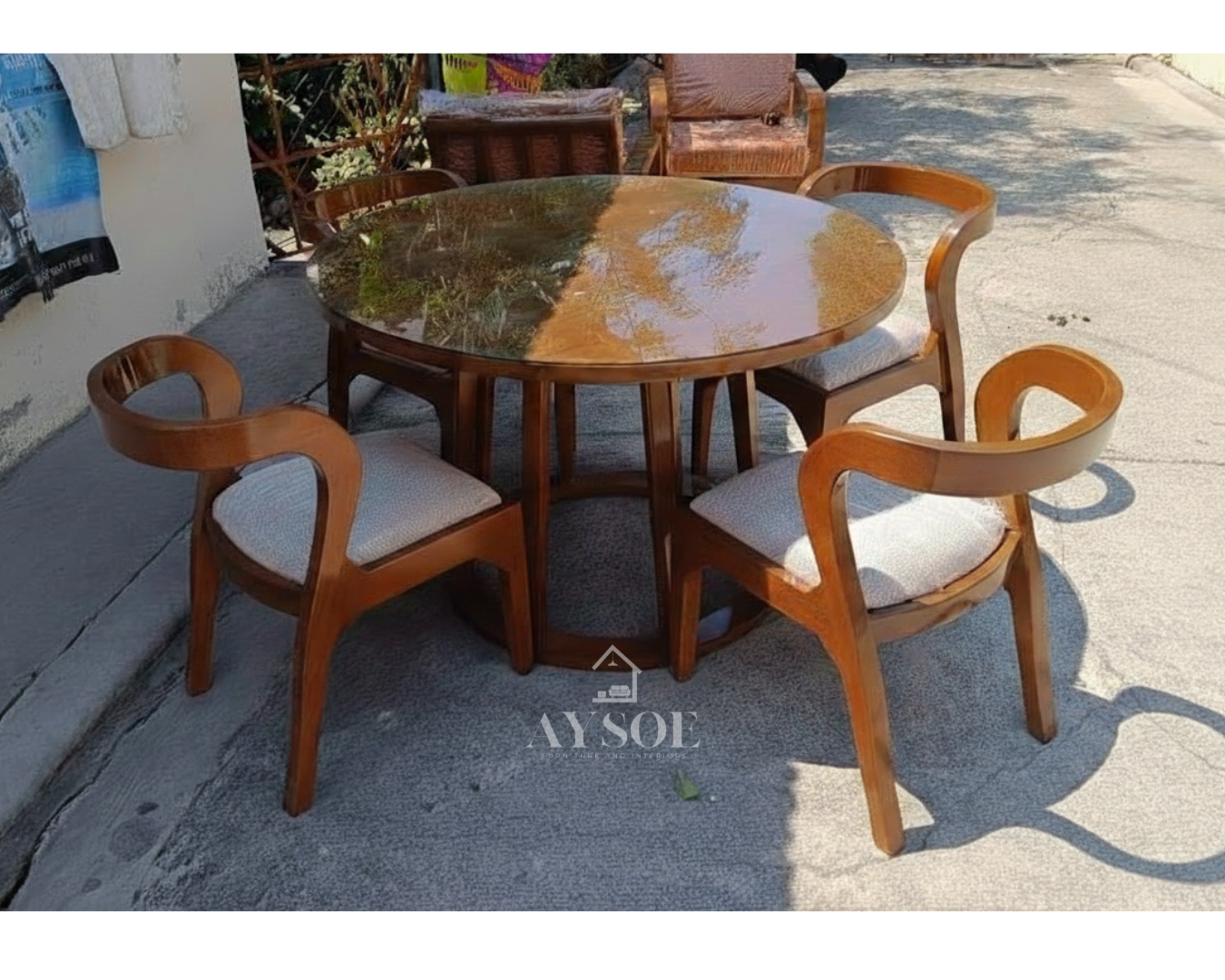 A round 4-seater dining set with a glossy tabletop on a drum-style wood base, plus four sculpted curved-back chairs with cream cushioned seats. Solid wood, wipe-clean, made to order.