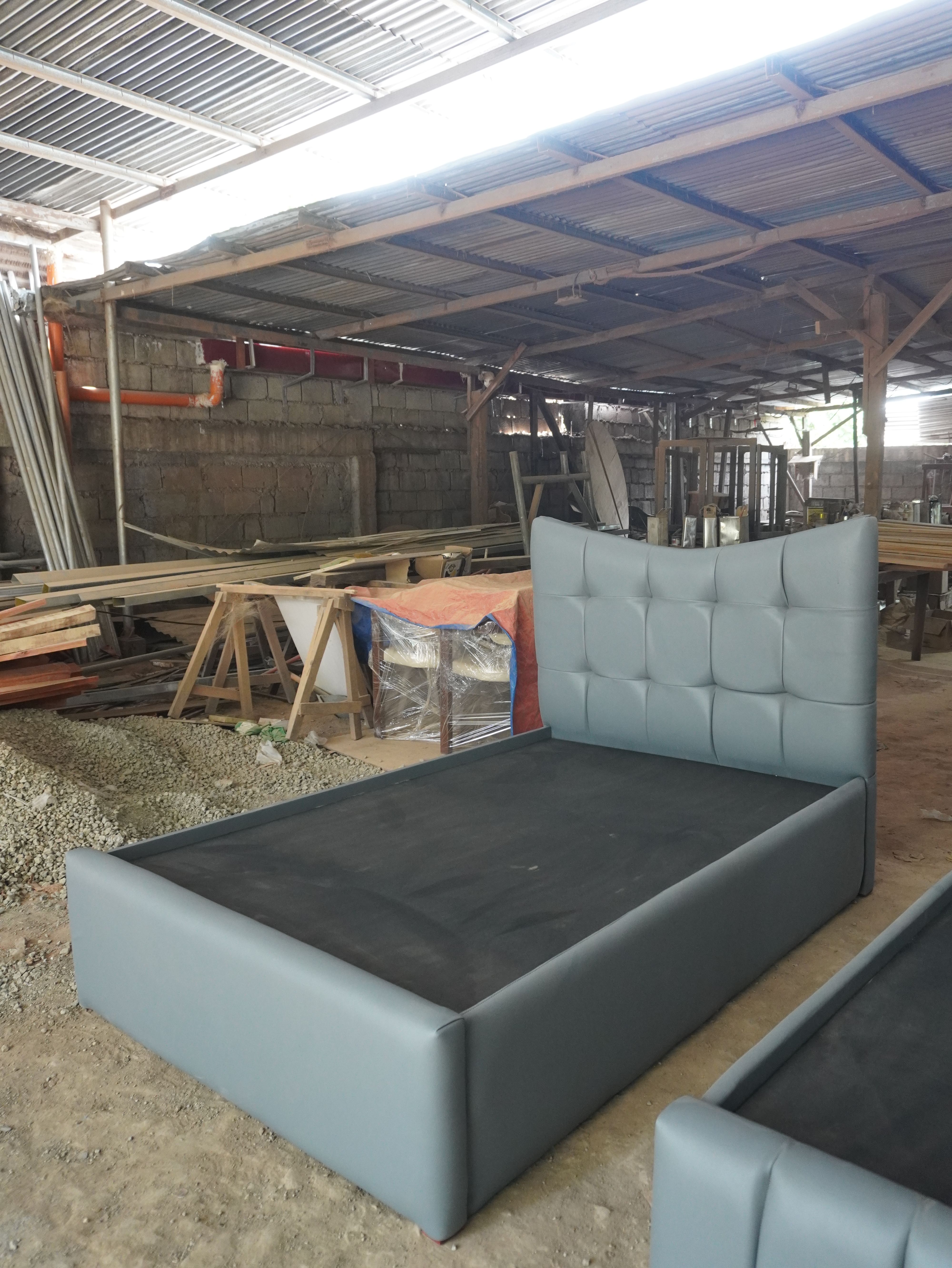 A modern upholstered bed in soft steel-blue leatherette, with a curved-top headboard of plush square tufted panels and a smooth, fully wrapped frame. Clean, distinctive, and easy to wipe clean.