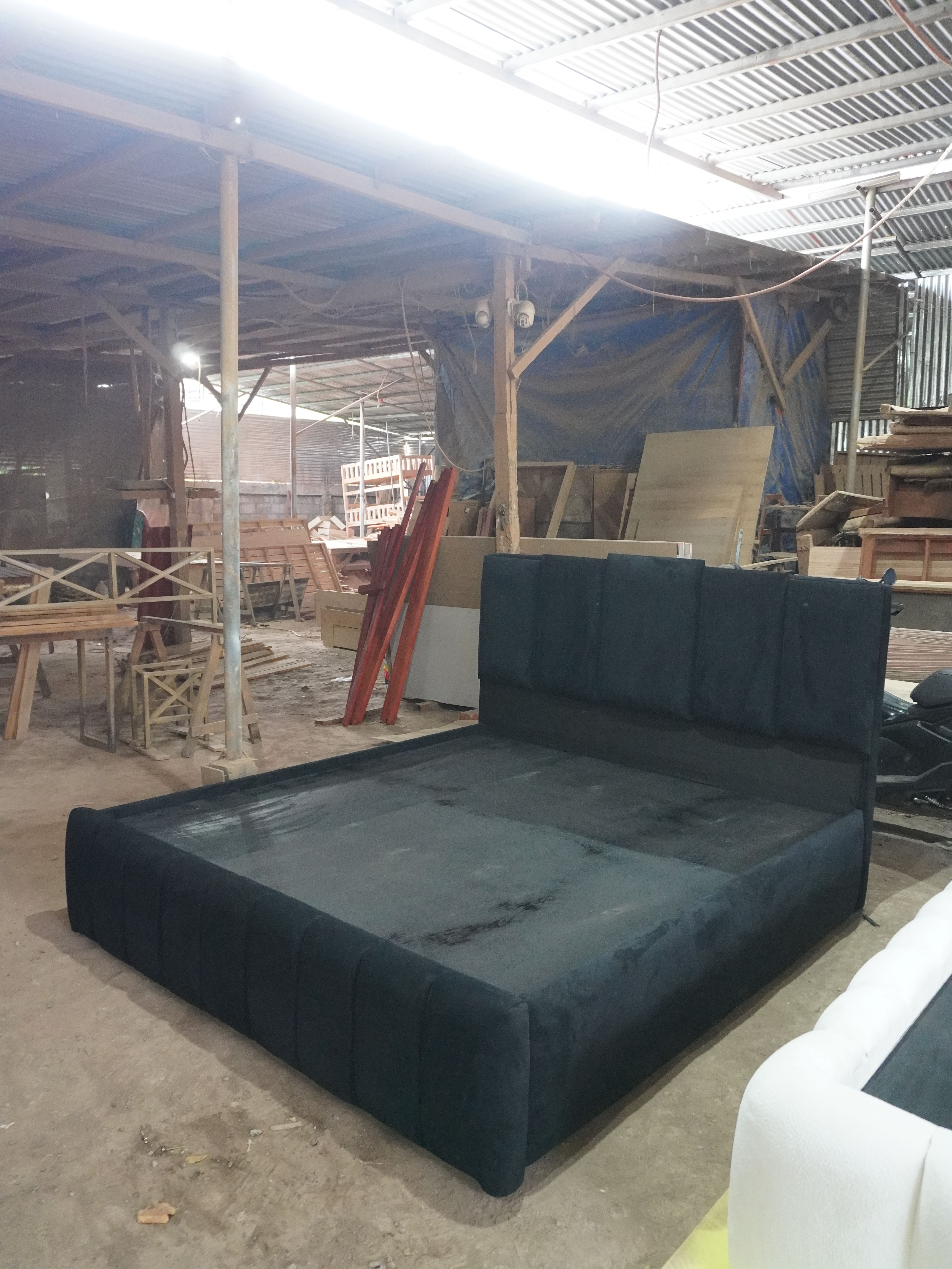 A bold black velvet-style bed with a tall headboard of five raised vertical panels in staggered heights, a channel-paneled footboard, and a fully wrapped frame. Dramatic, modern, and made to stand out.