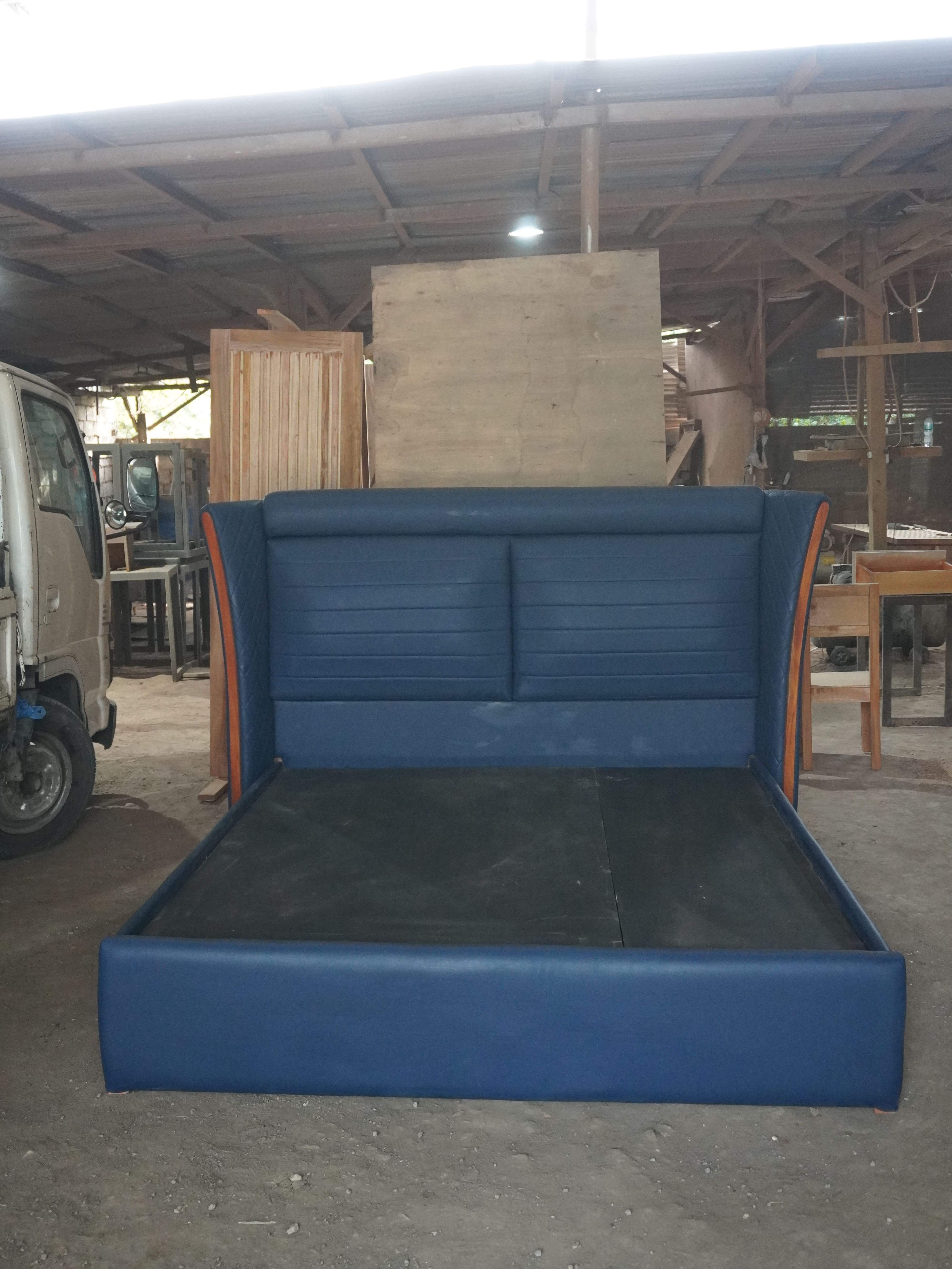 A bold navy blue leatherette bed with a tall curved wingback headboard, horizontal channel panels, and quilted diamond-stitch wings edged in warm wood. Clean, fully wrapped frame with a solid platform base.