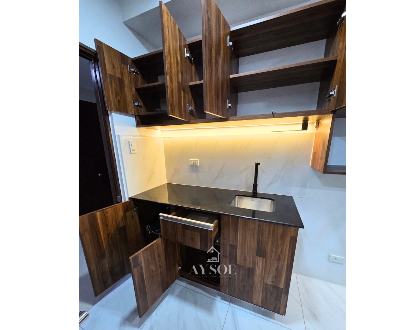 A compact walnut-finish kitchenette with upper and lower cabinets, plus a floating bar counter with a fluted wood wall panel and pendant lights. Made for condos and studio units.