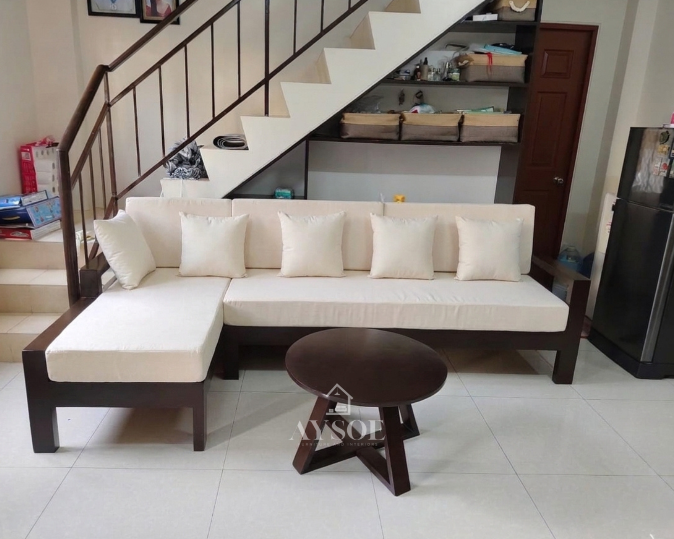 An L-shaped chaise sofa on a dark espresso wood frame with thick cream cushions and five throw pillows, plus a round coffee table with a star-shaped base. Bright, clean, and made to order.