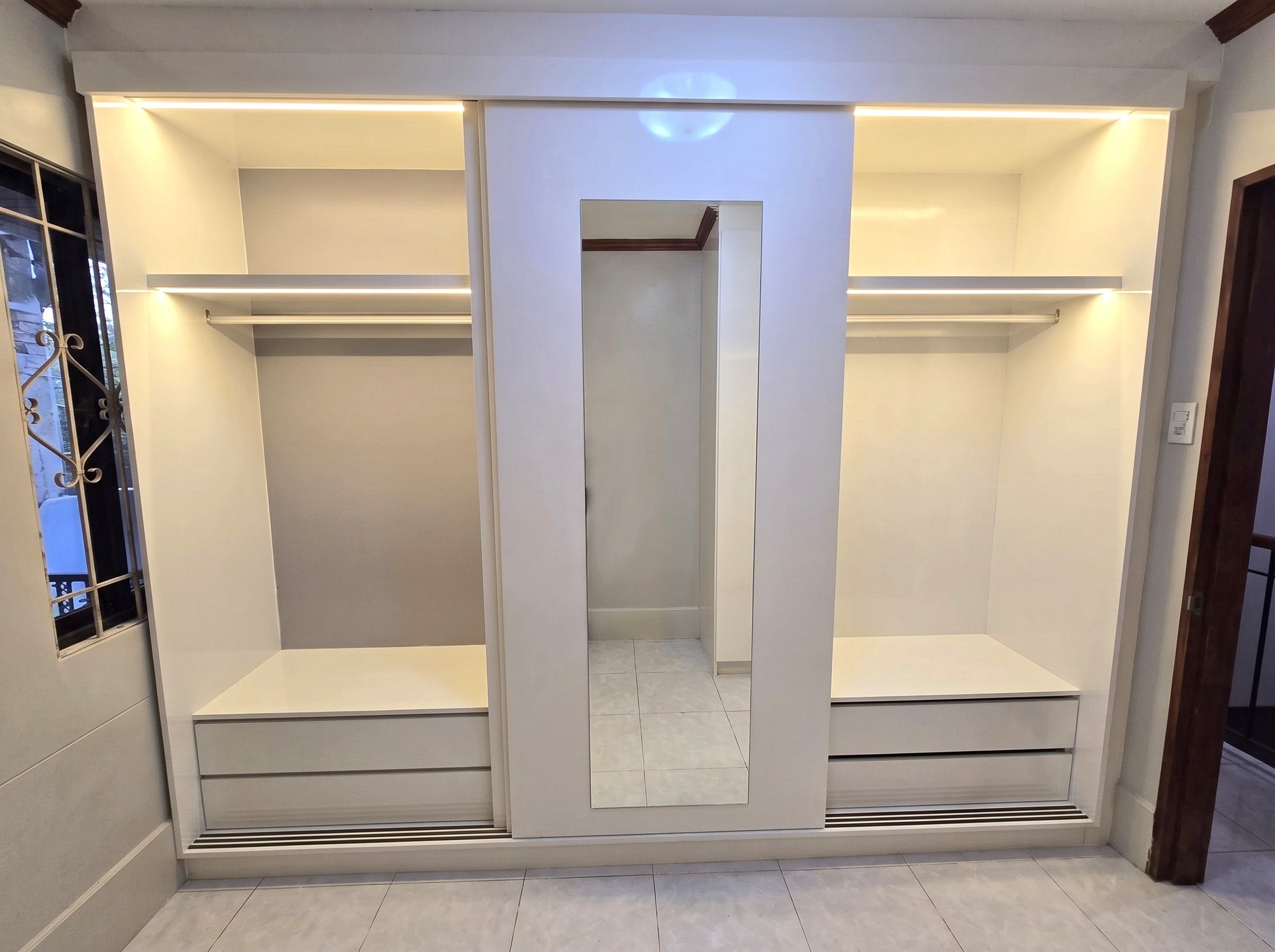 A white built-in wardrobe with a sliding mirror-panel door, two wide hanging sections, four deep drawers, and warm LED lighting inside. Made to fit your wall.