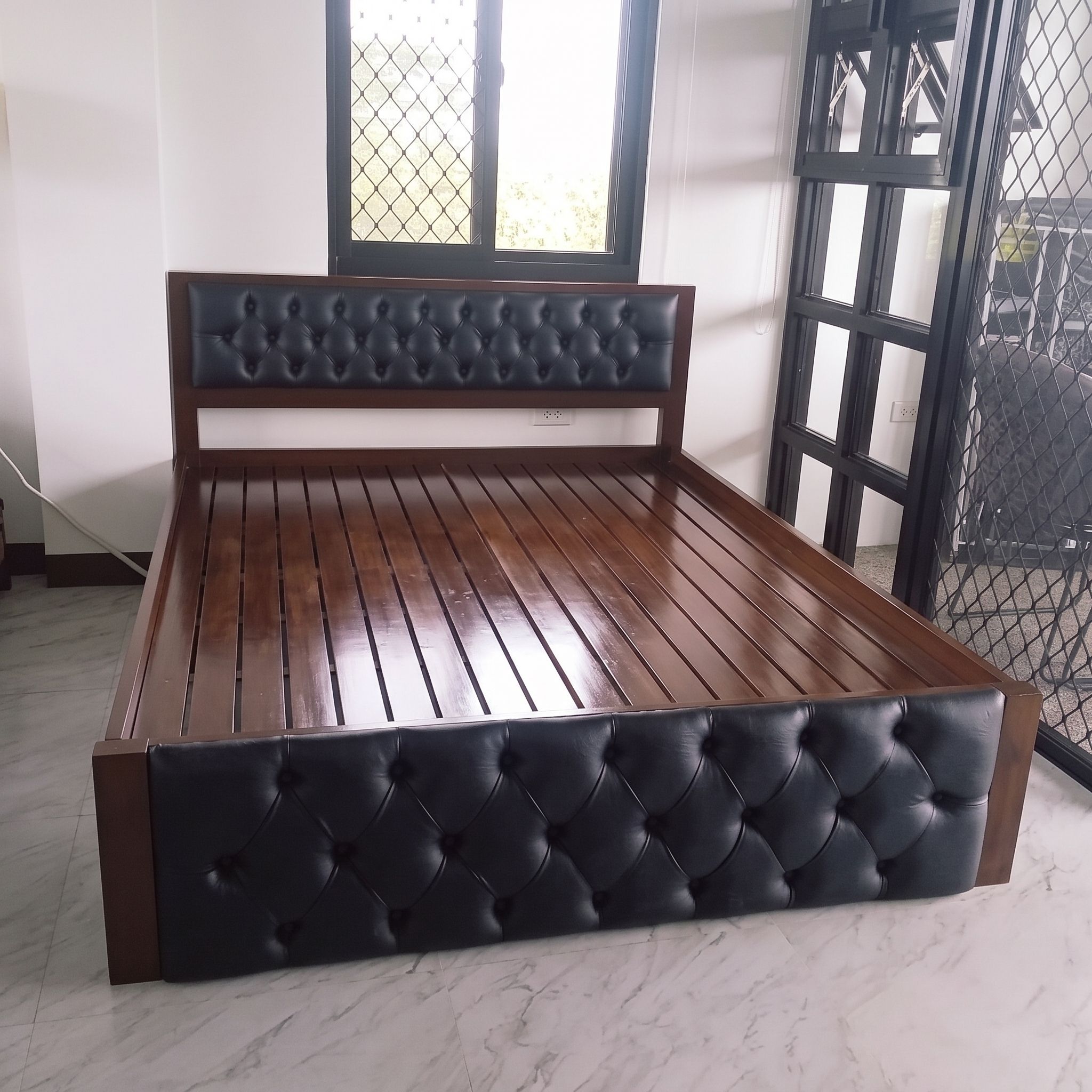 A solid wood bed in a rich, glossy dark walnut finish, with a black button-tufted leatherette headboard panel, a matching tufted footboard, and a sturdy slatted base. Bold, classic, and built to last.