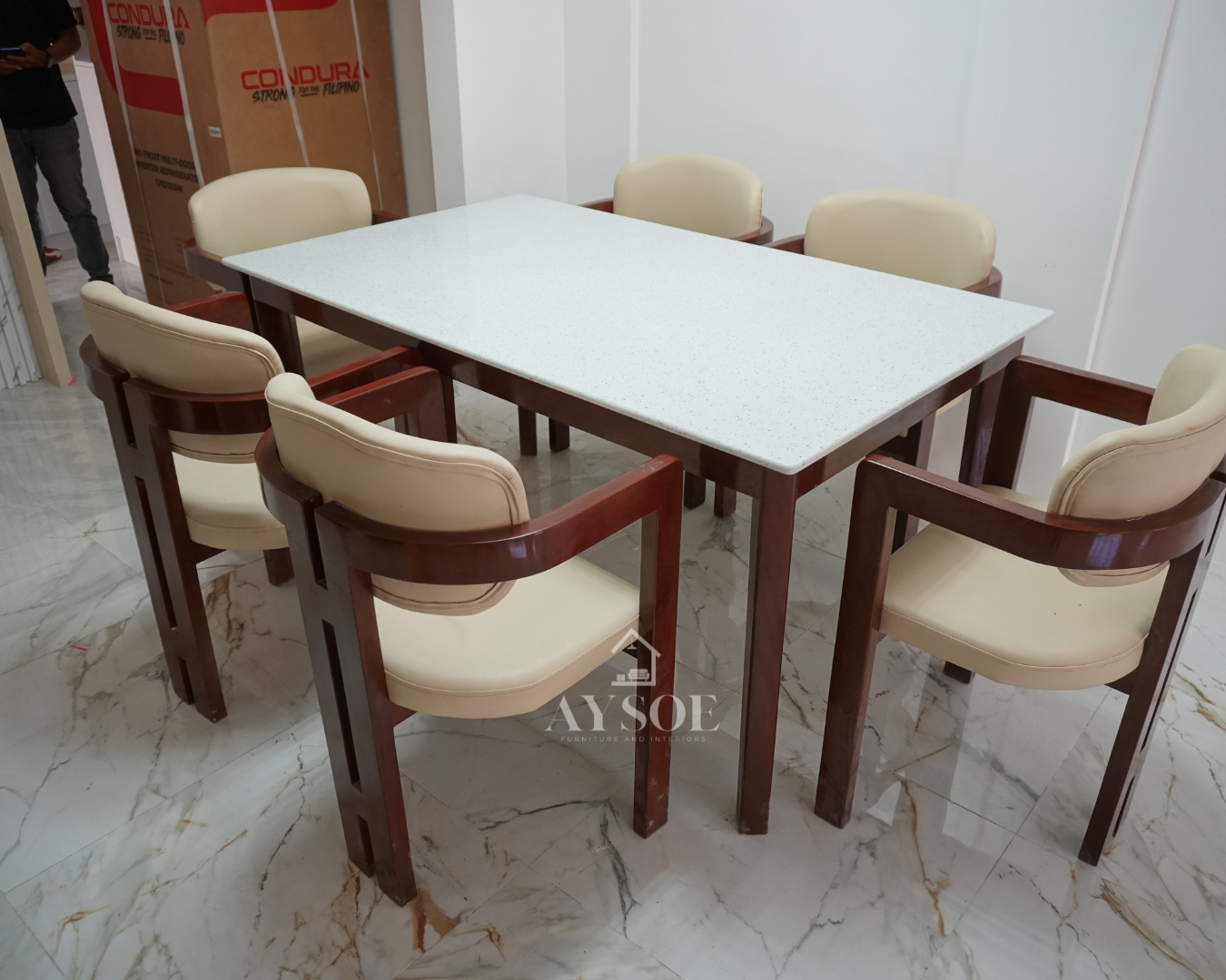 A 6-seater dining set with a white speckled stone-look tabletop on a glossy mahogany wood base, plus six curved-back armchairs with cream leatherette cushions. Elegant, wipe-clean, made to order.