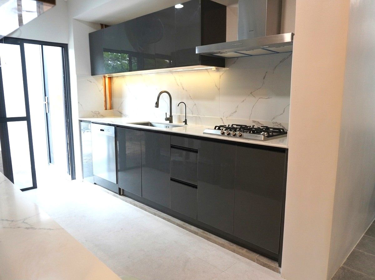 A sleek single-wall kitchen in high-gloss charcoal with a Calacatta-style marble backsplash. Handleless cabinetry, integrated appliances, and warm under-cabinet lighting give it a clean, modern look.