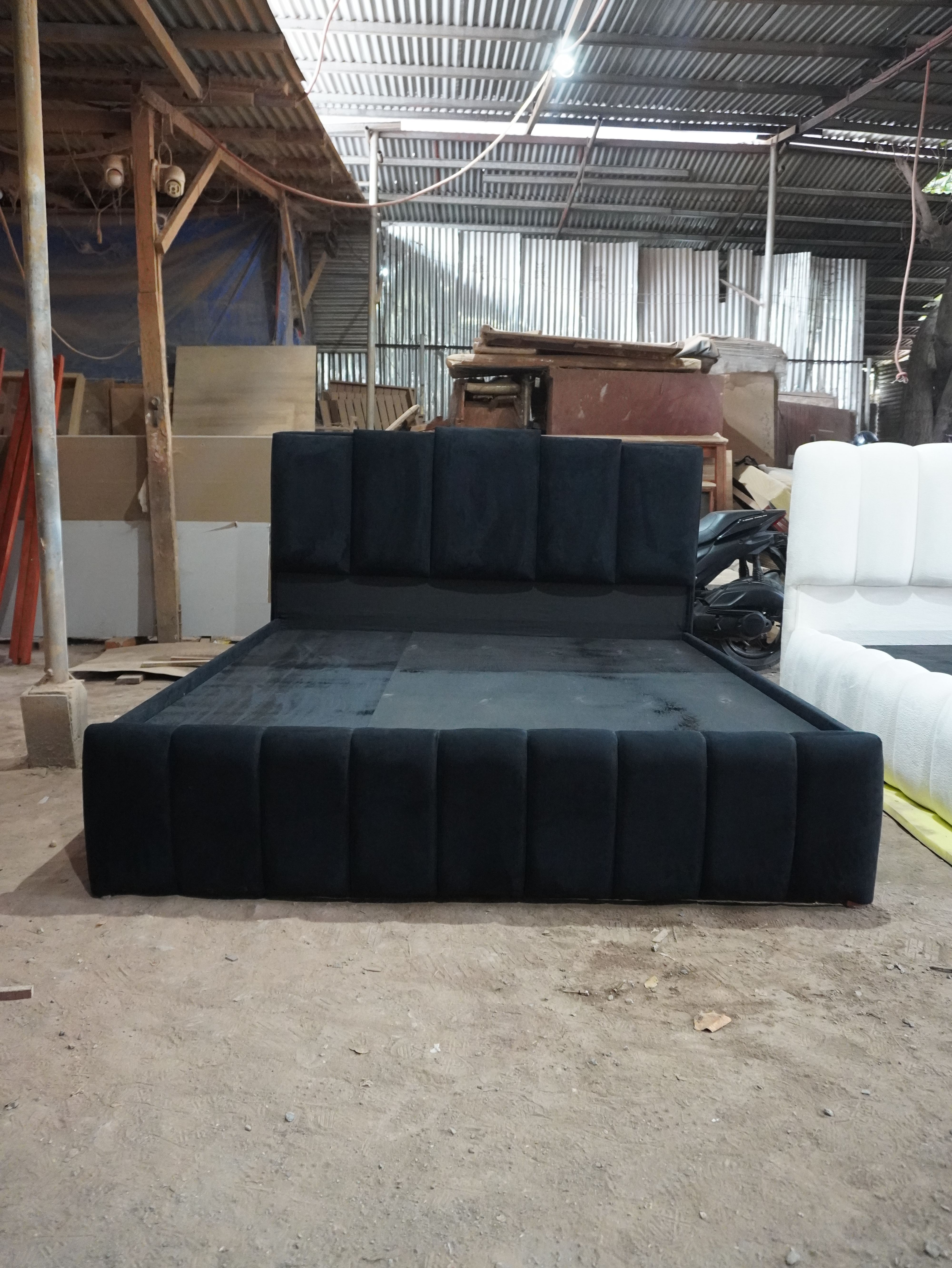 A bold black velvet-style bed with a tall headboard of five raised vertical panels in staggered heights, a channel-paneled footboard, and a fully wrapped frame. Dramatic, modern, and made to stand out.