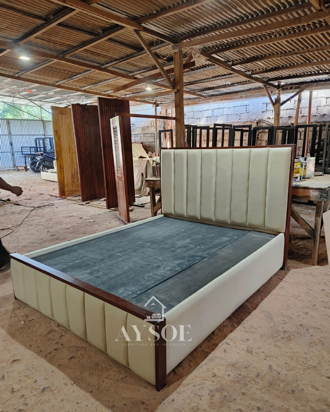 A platform bed frame in cream leatherette, with a tall channel-tufted headboard, a matching footboard, and dark mahogany wood trim. Clean, elegant, and built to last.