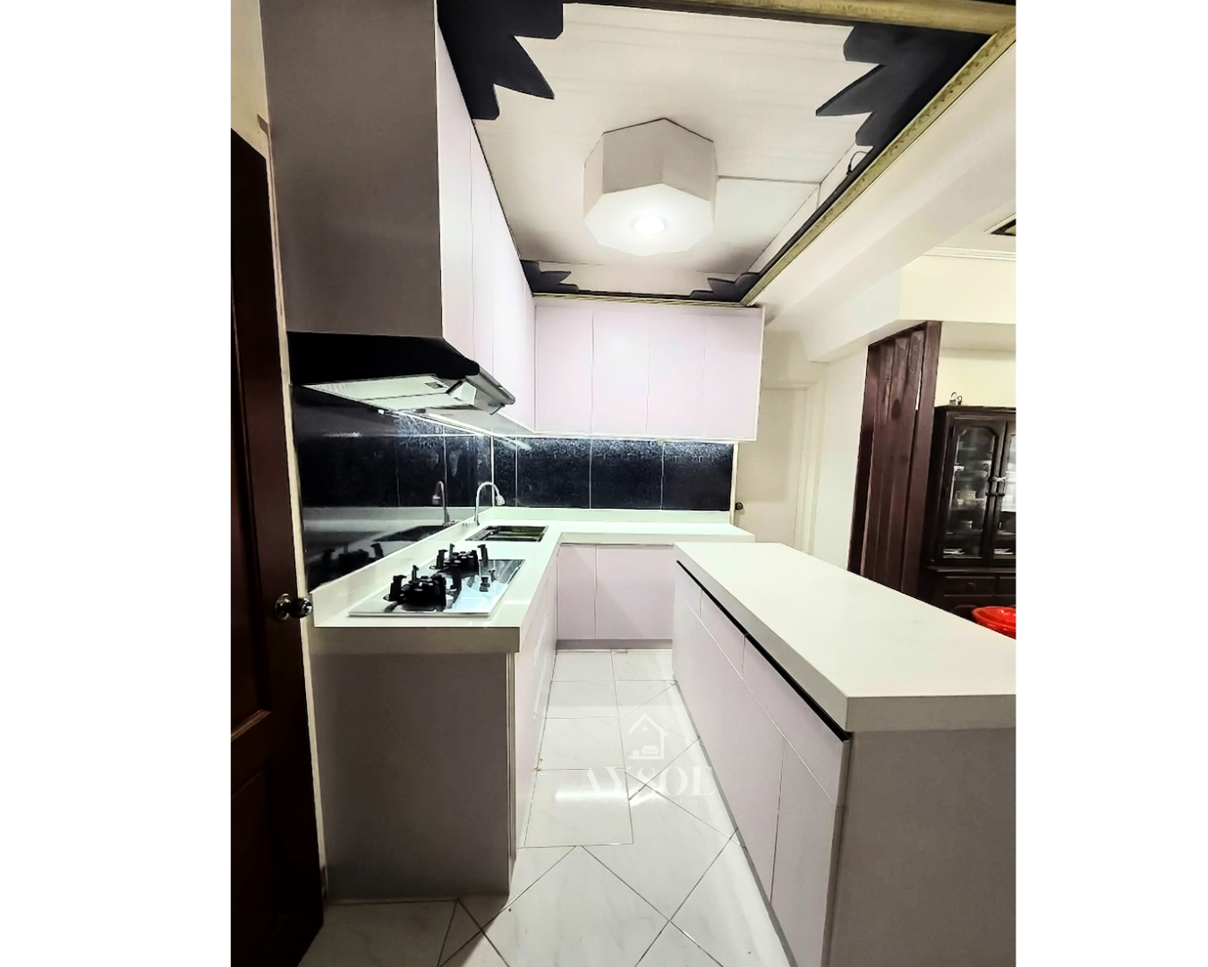 A modern L-shaped kitchen set with handleless white cabinets, a marble-look countertop, a black glass backsplash, and a fluted island. Clean, bright, and full of storage.