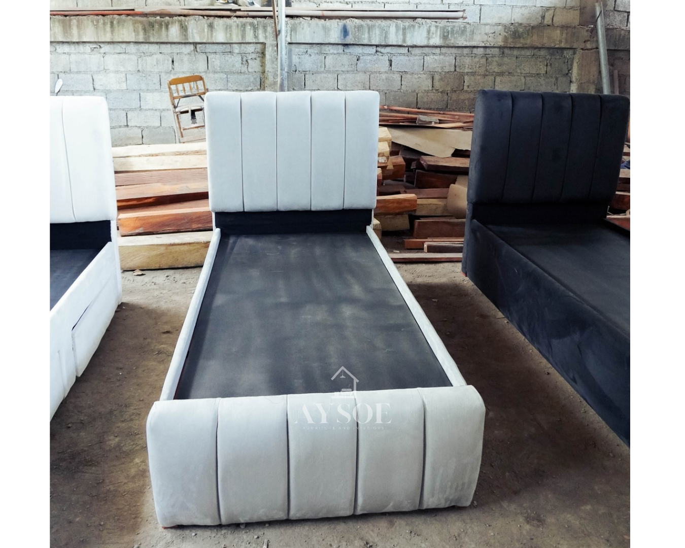 A single bed frame upholstered in soft light grey fabric, with a channel-tufted headboard and footboard and two roomy pull-out drawers. Stylish and space-saving.