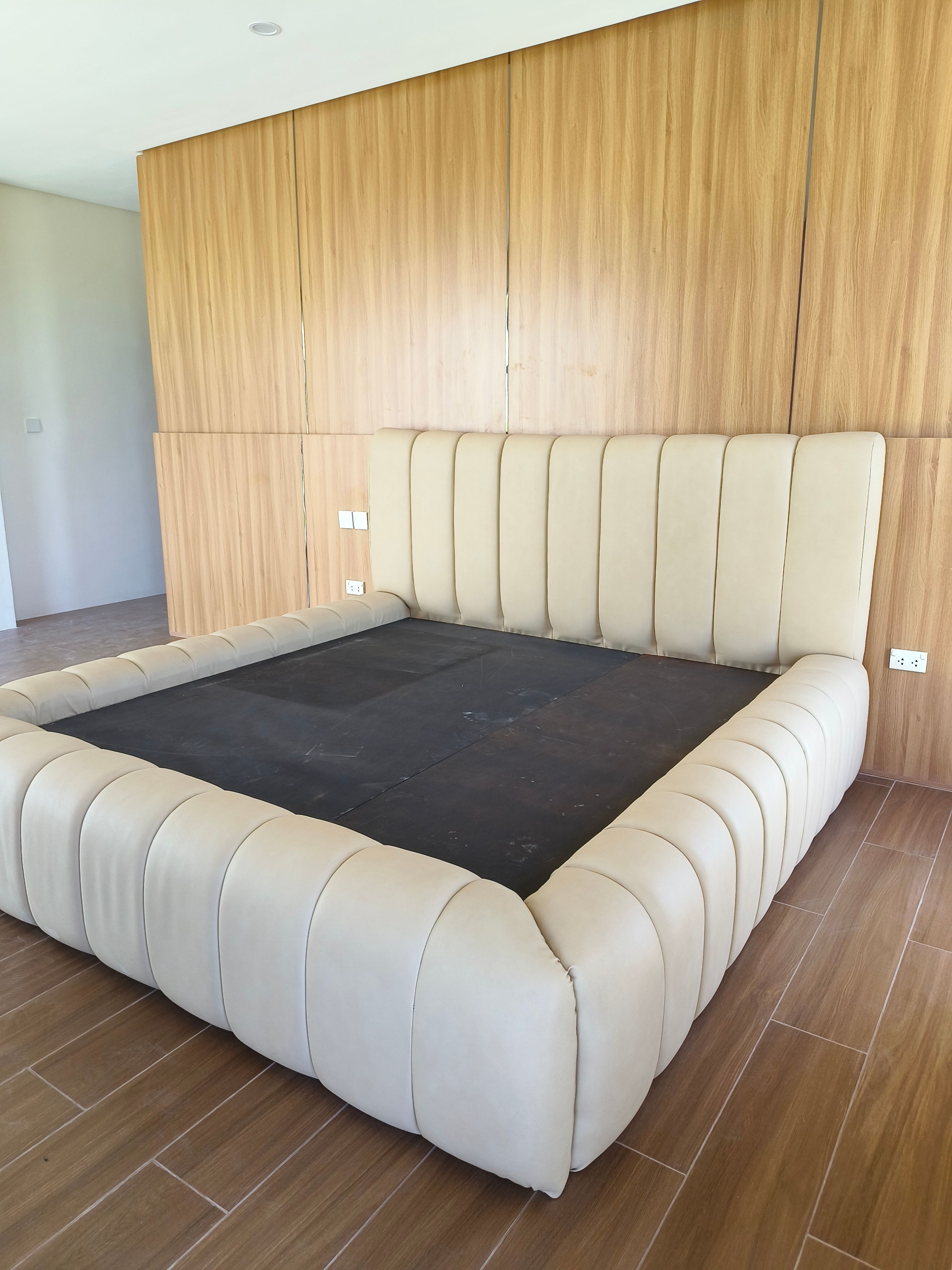 A soft, sculptural bed in smooth cream leatherette, with a tall wide channel headboard and thick pillow-style channels wrapping the whole frame. Plush, modern, and easy to wipe clean.