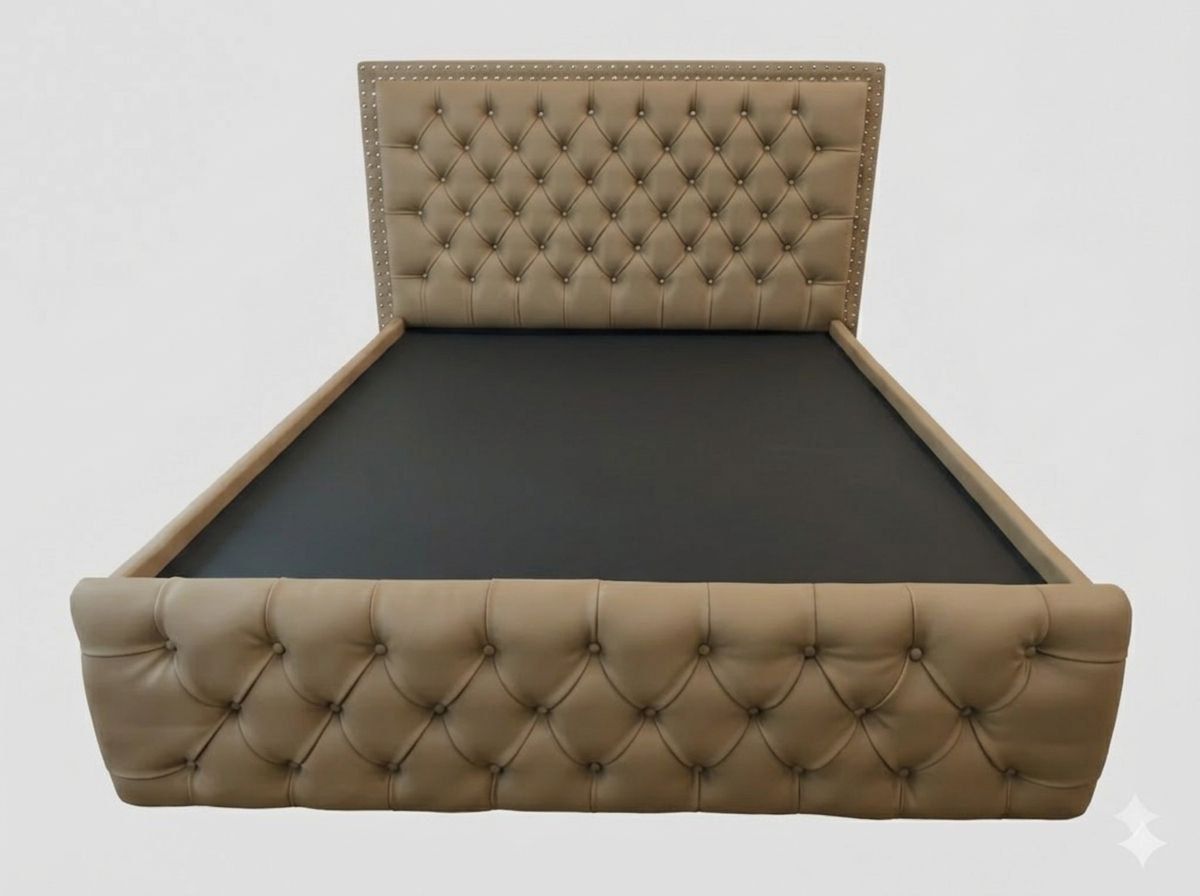 The mahogany frame is upholstered in a light cream or tan leatherette. It retains the signature diamond button-tufting on both the headboard and the footboard, accented with small metal nailhead trim along the borders.