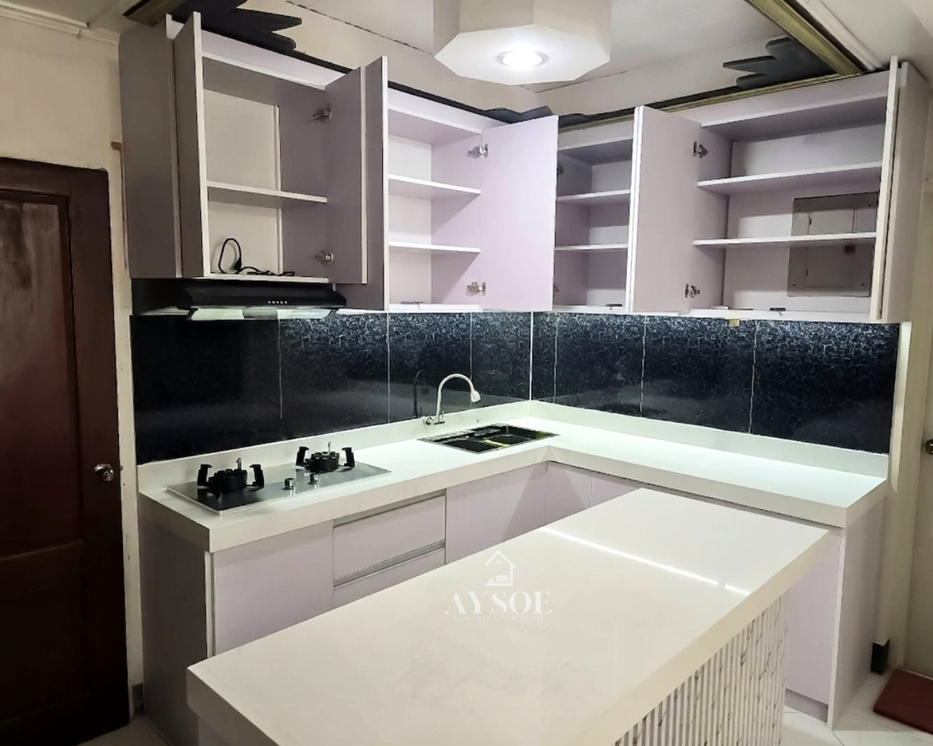 A modern L-shaped kitchen set with handleless white cabinets, a marble-look countertop, a black glass backsplash, and a fluted island. Clean, bright, and full of storage.