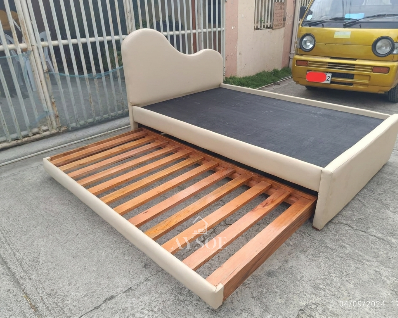 A single bed frame in soft cream leatherette, with a wavy cloud-shaped headboard and a pull-out trundle bed underneath. Two beds in one, great for kids and small rooms.