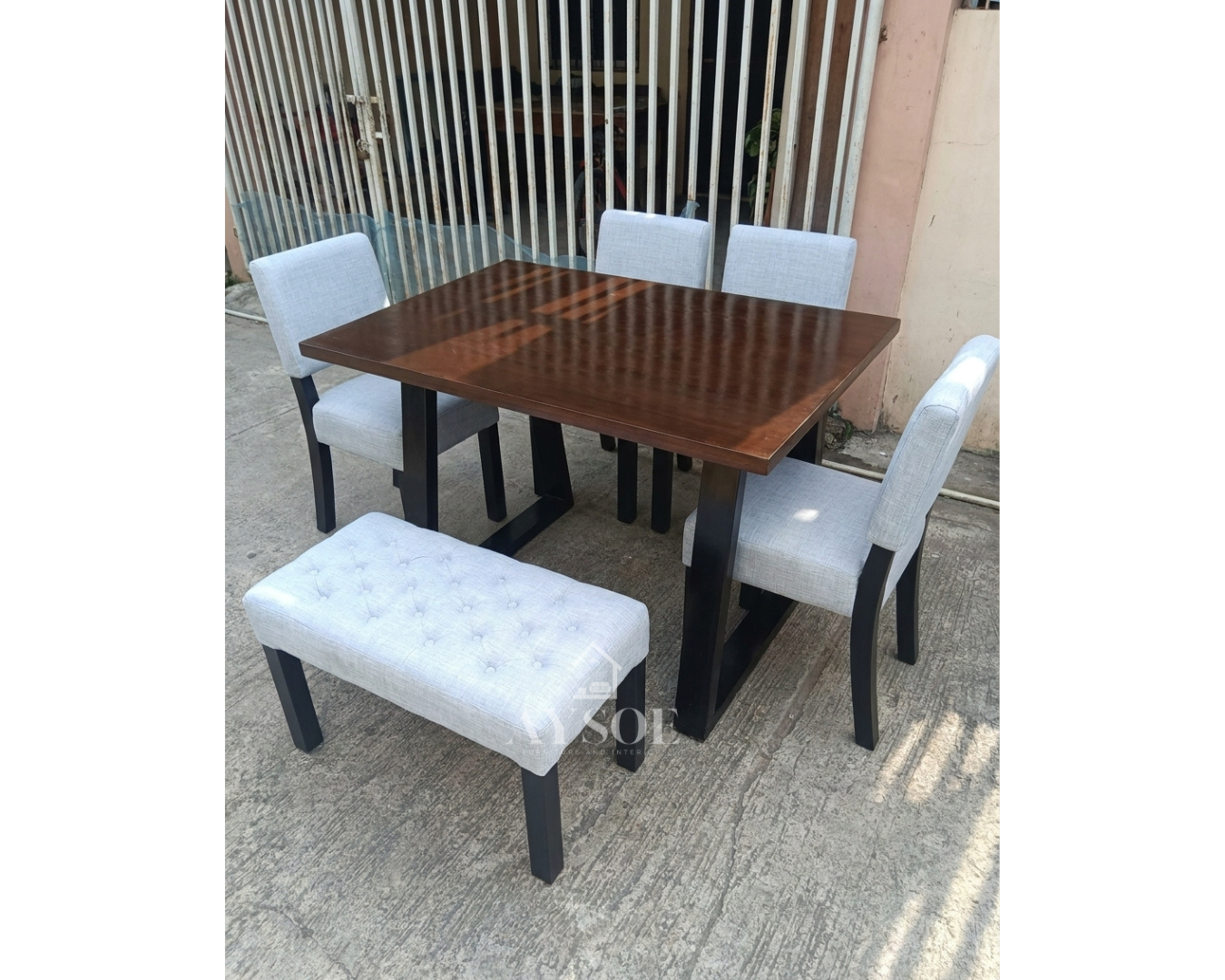 A modern dining set with a dark walnut wood top, bold black trapezoid legs, four light grey upholstered chairs, and a matching tufted bench. Comfortable, stylish, made to order.