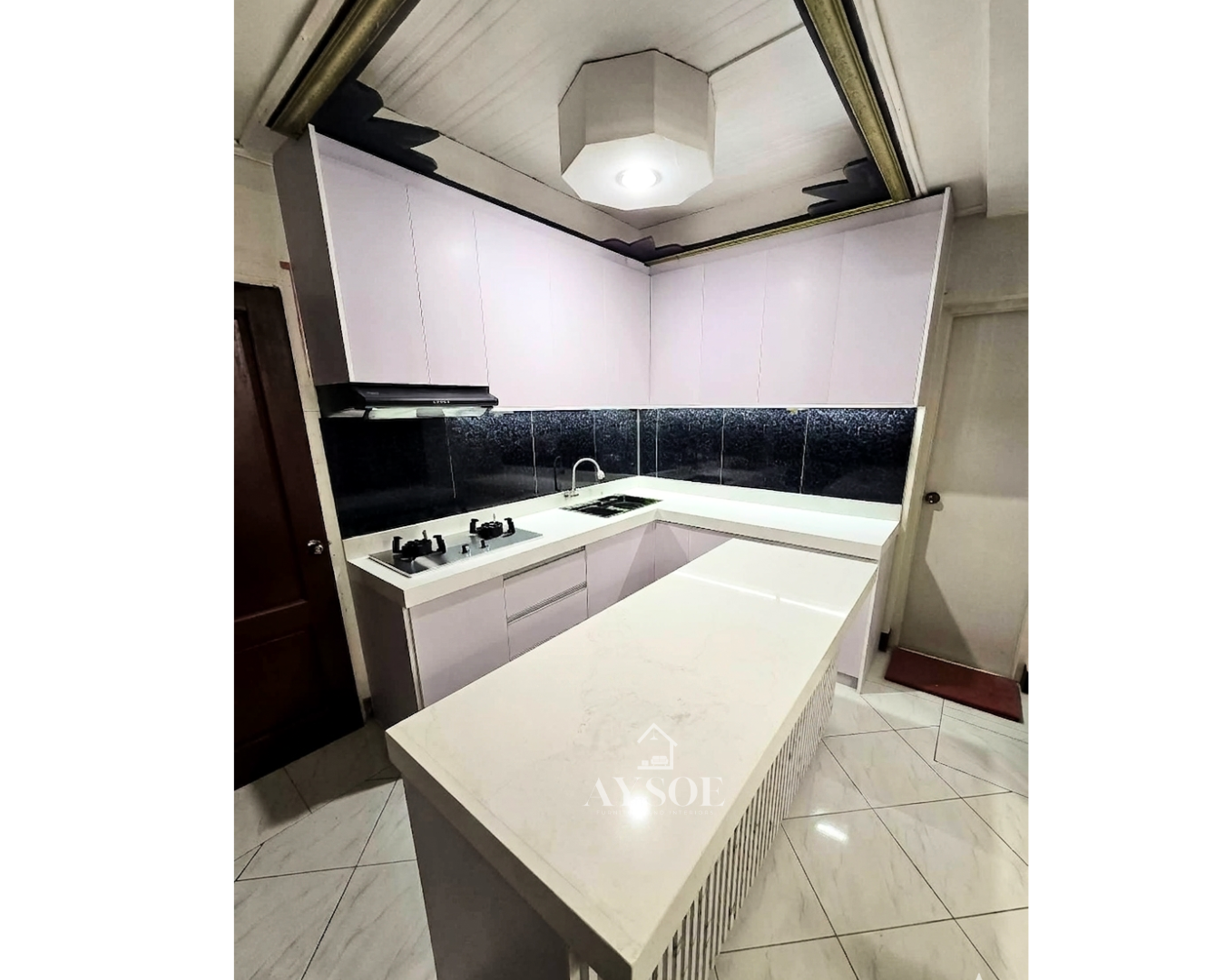 A modern L-shaped kitchen set with handleless white cabinets, a marble-look countertop, a black glass backsplash, and a fluted island. Clean, bright, and full of storage.