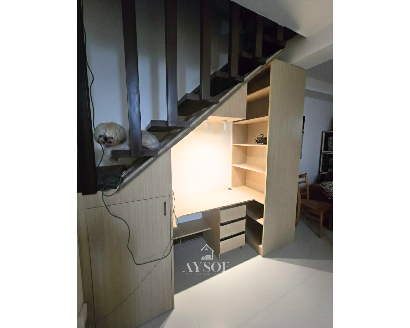 A custom under-stair desk nook in a light oak wood-grain finish, with a built-in desk, three drawers, a tall bookshelf, and a storage cabinet. Turns unused stair space into a home office.