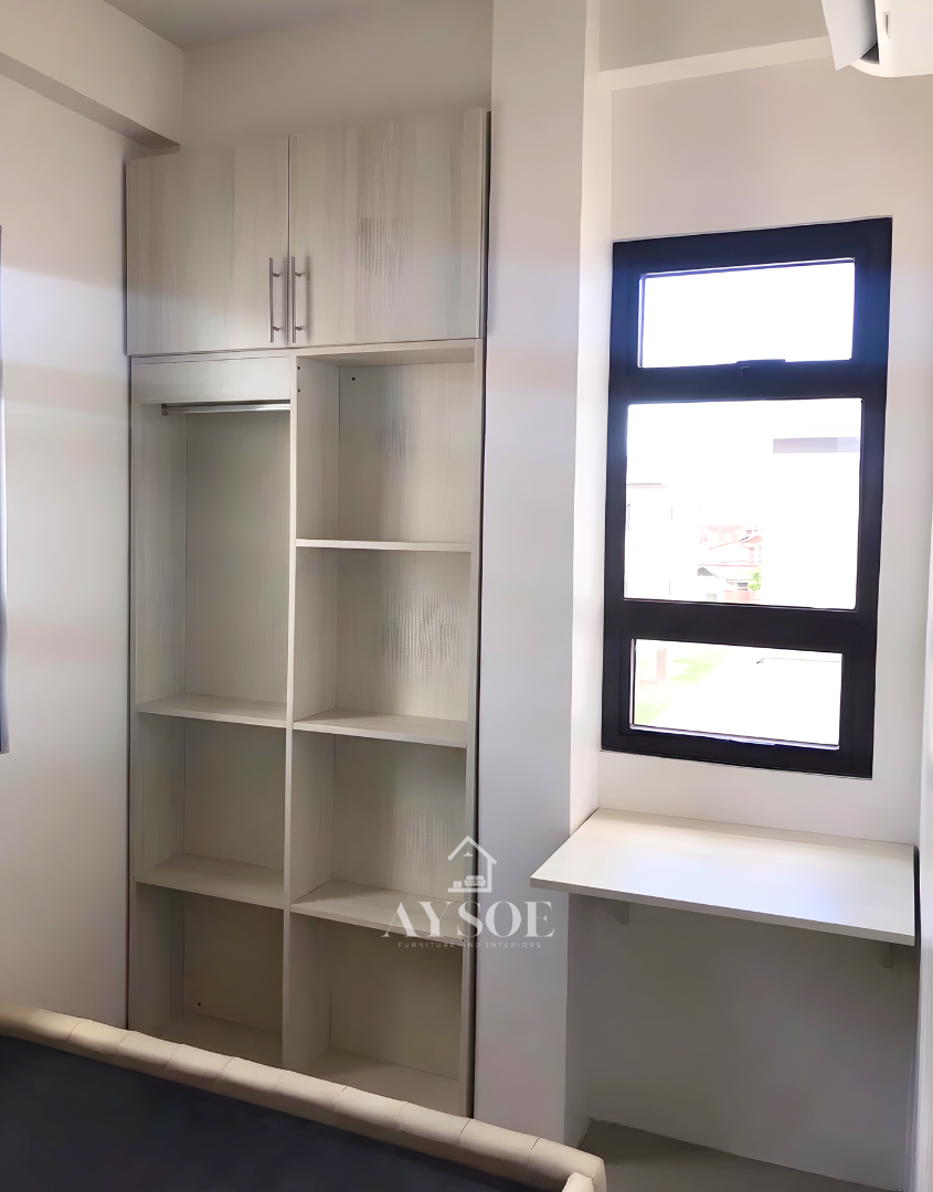 A custom space-saving wardrobe in a light oak wood-grain finish, with a hanging rod, open shelves, an overhead cabinet, and a floating desk. Smart storage for small bedrooms.