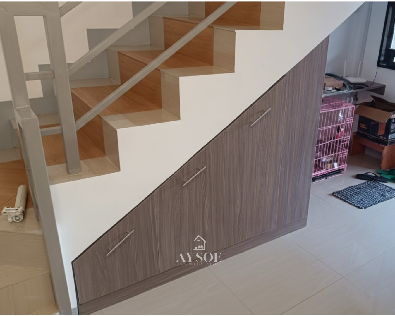 A custom under-stair storage cabinet with three deep pull-out drawers in a grey-brown wood-grain finish. Turns unused stair space into organized storage.