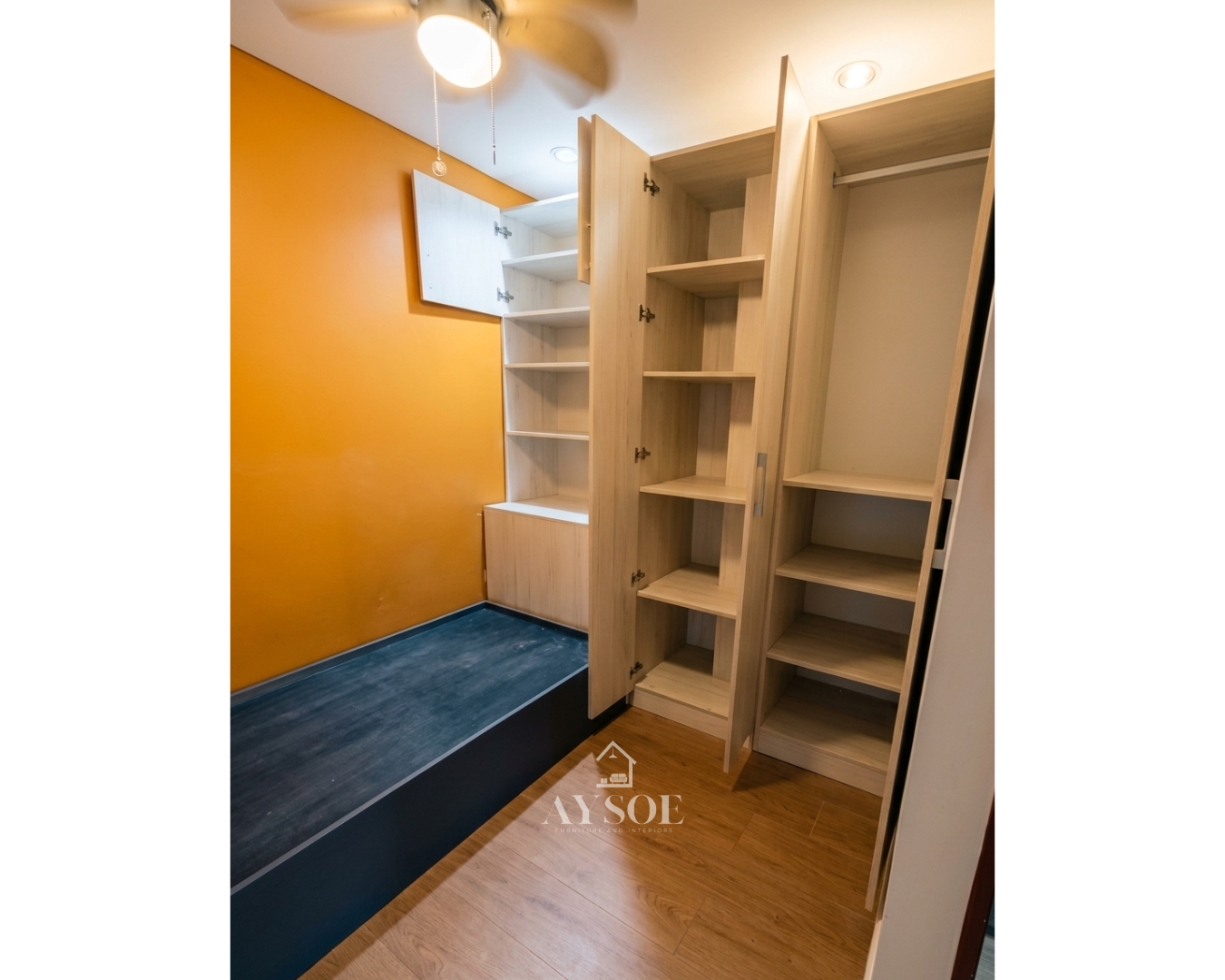 A custom light oak storage set with a tall wardrobe and a built-in shelf unit with overhead and lower cabinets. Smart storage for small rooms.