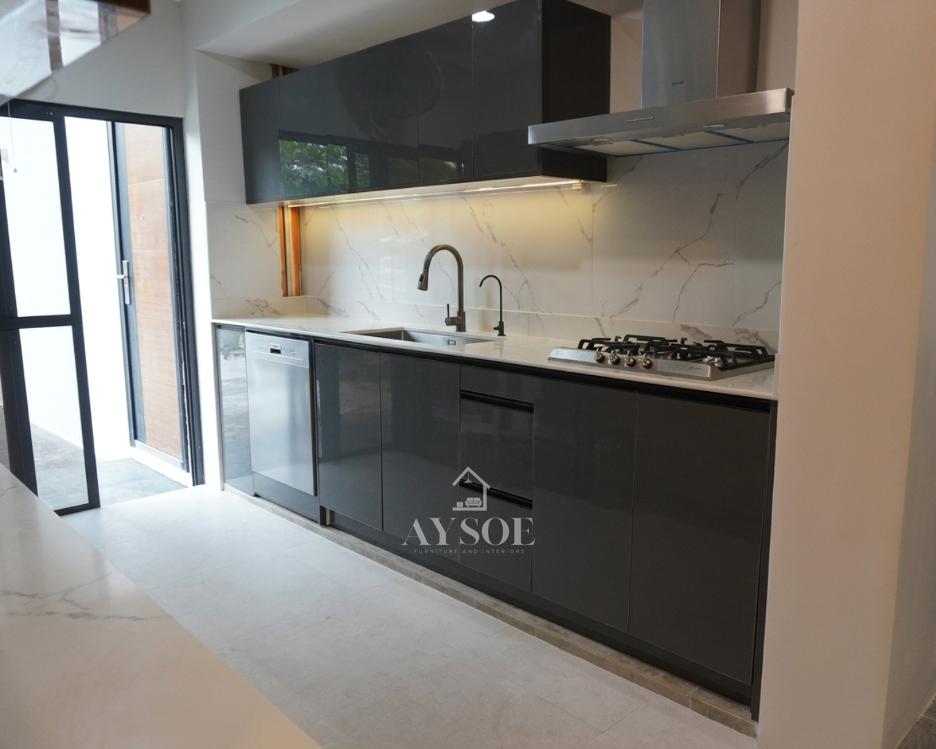 A sleek single-wall kitchen in high-gloss charcoal with a Calacatta-style marble backsplash. Handleless cabinetry, integrated appliances, and warm under-cabinet lighting give it a clean, modern look.