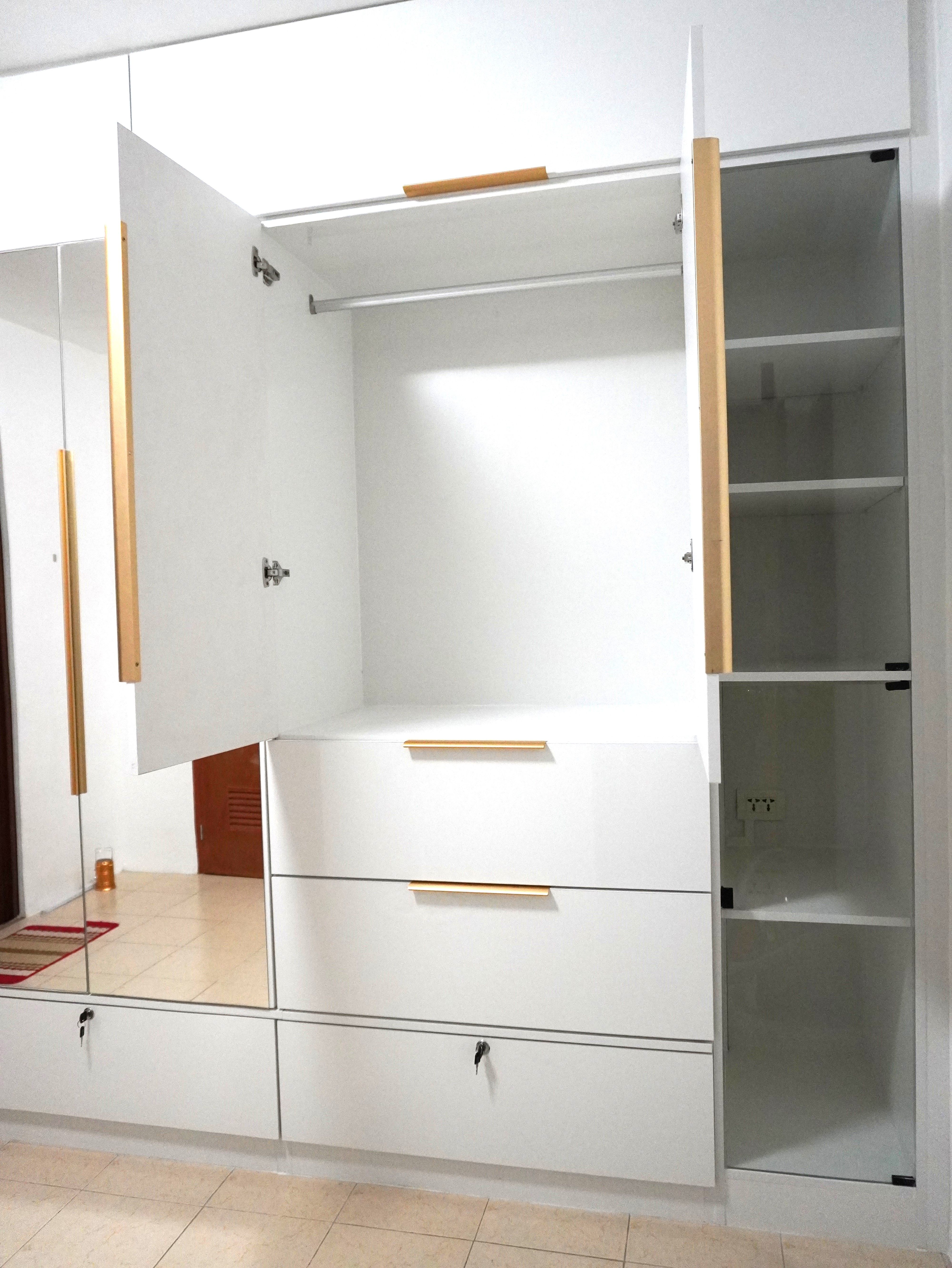 A floor-to-ceiling built-in wardrobe in high-gloss white, with gold bar handles, a full-height center mirror, roomy drawers, three locking drawers, and glass-door shelving. Made to fit your wall.