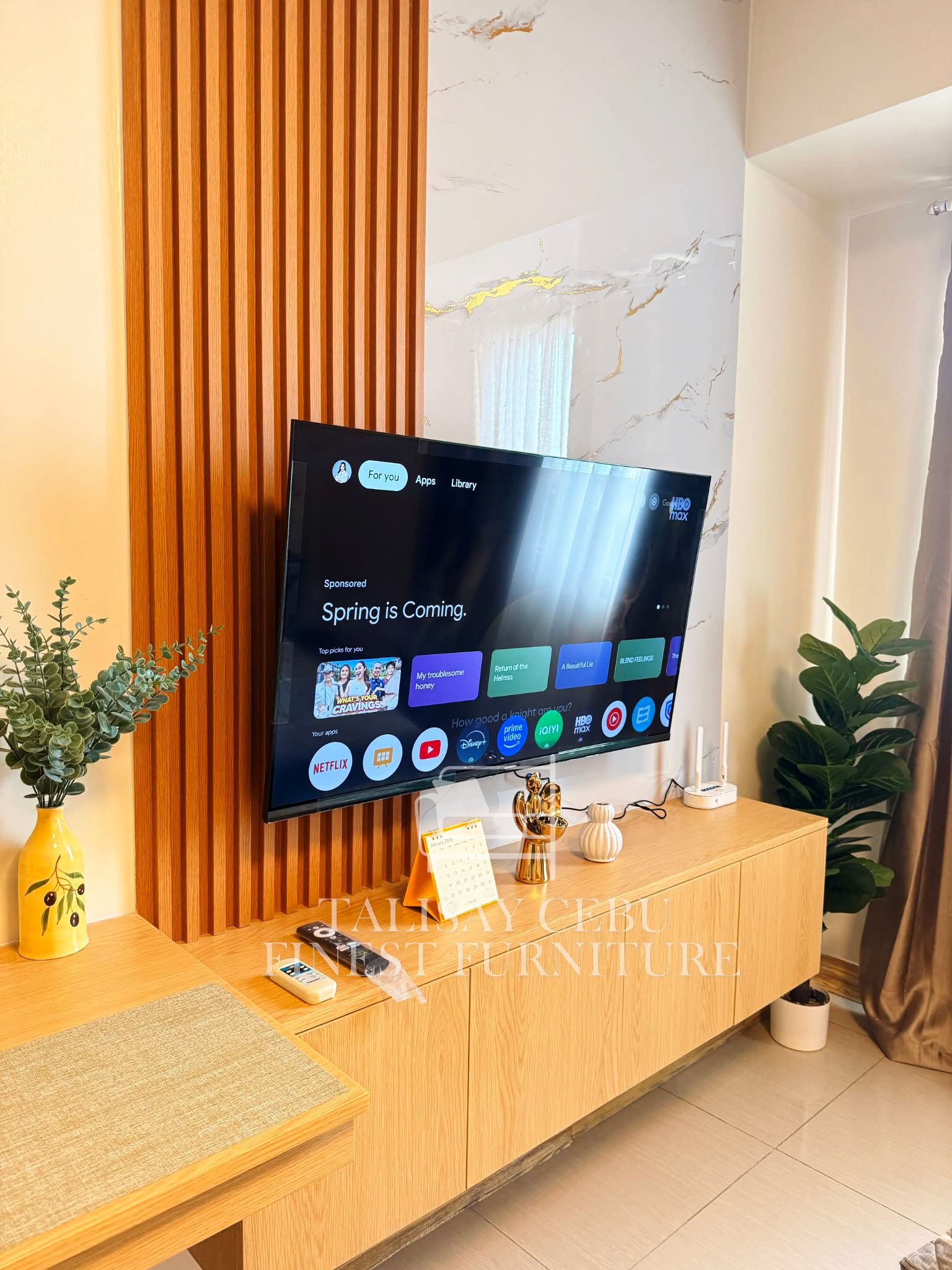 A wall-mounted TV set against wood-slat paneling and a gold-veined marble-look wall, with a built-in wood-grain console below.